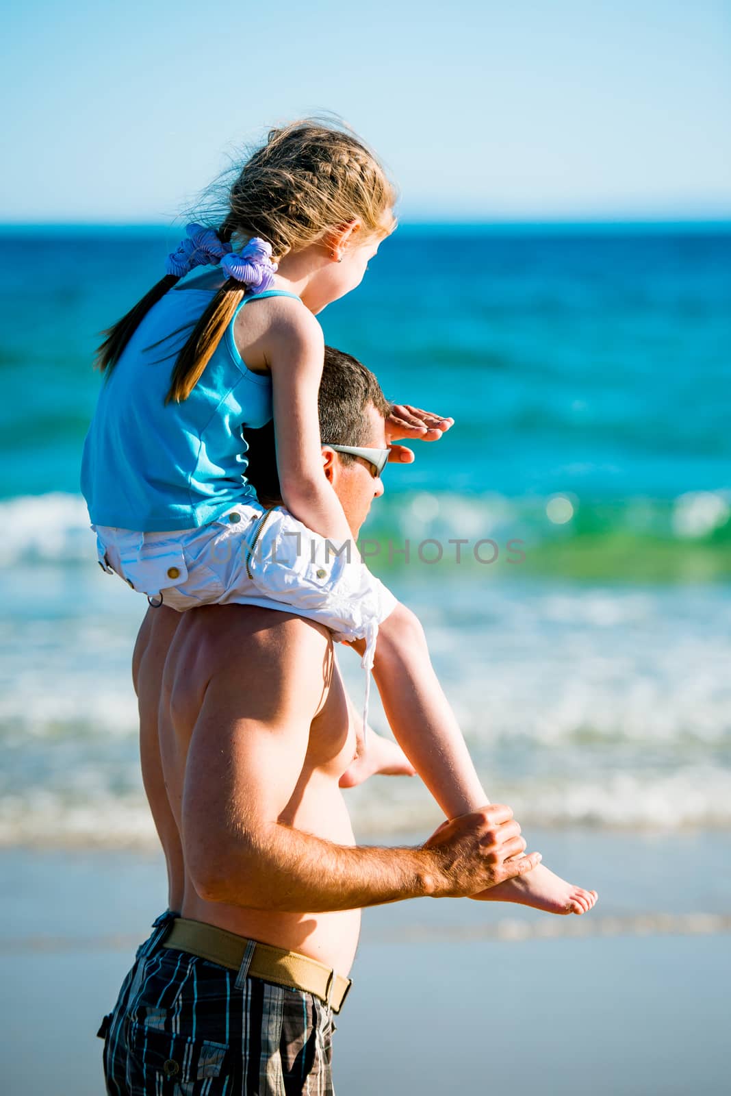 Father holding daughter on his shoulders and looking into the distance on the sea shore