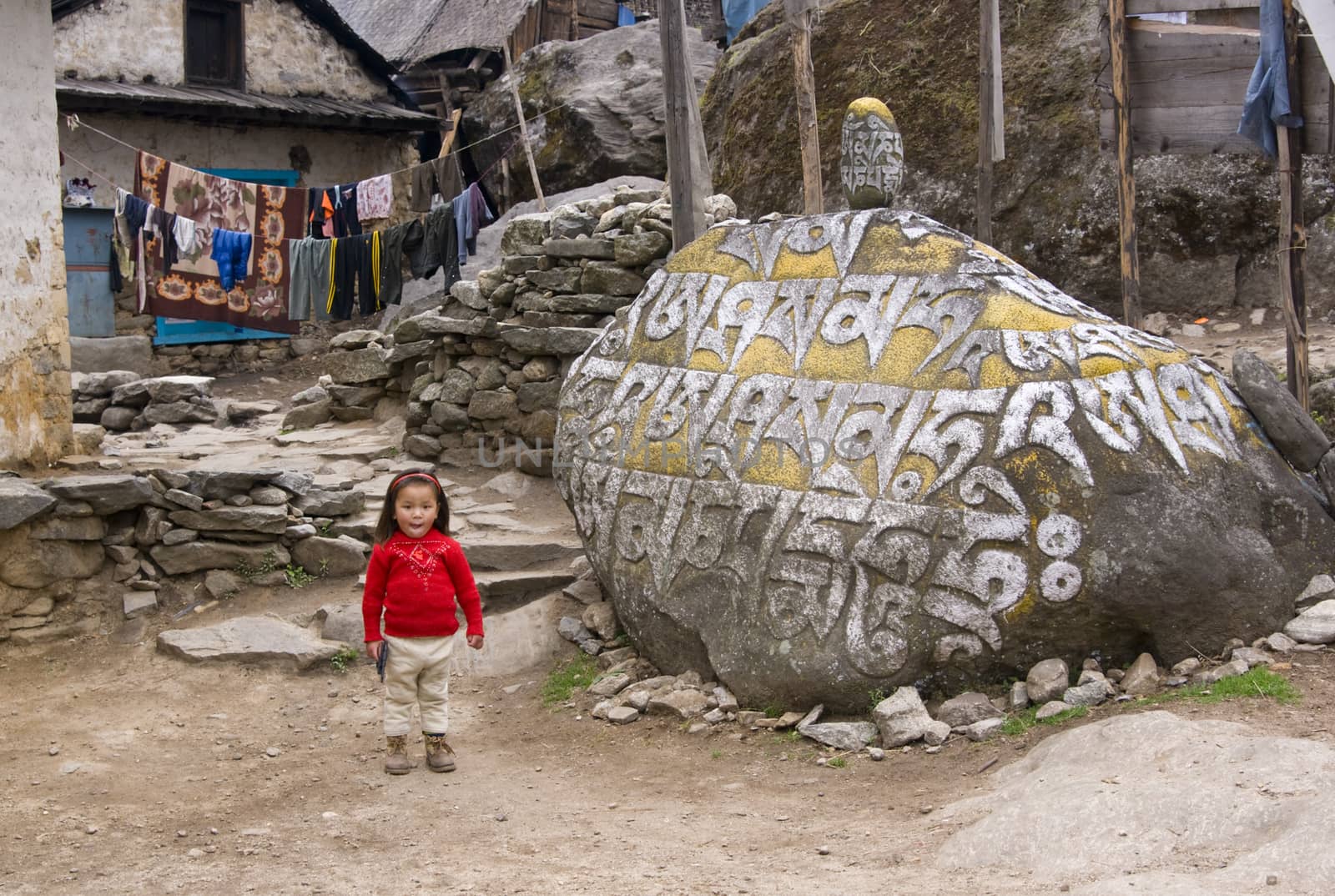Small girl armed with a toy gun standing by a large stone inscribed with Buddhist text on the path to Everest Base Camp in the Himalaya Mountains, Nepal