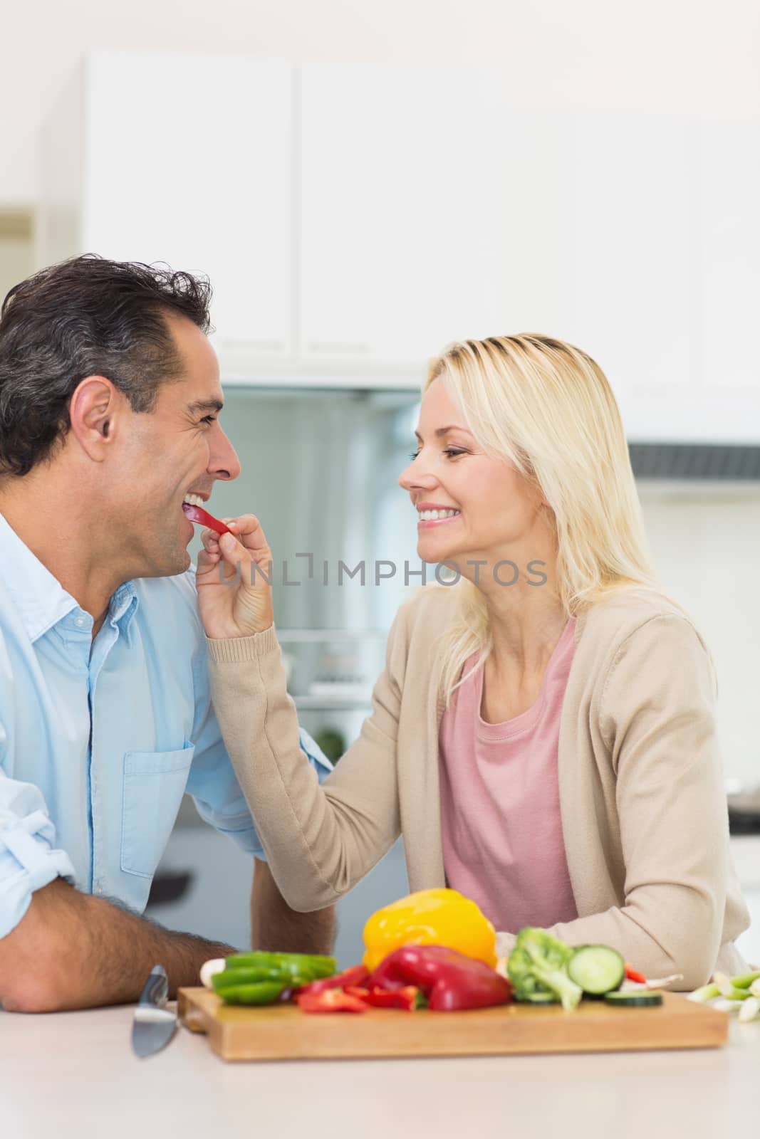 Happy loving woman feeding man vegetable in the kitchen at home