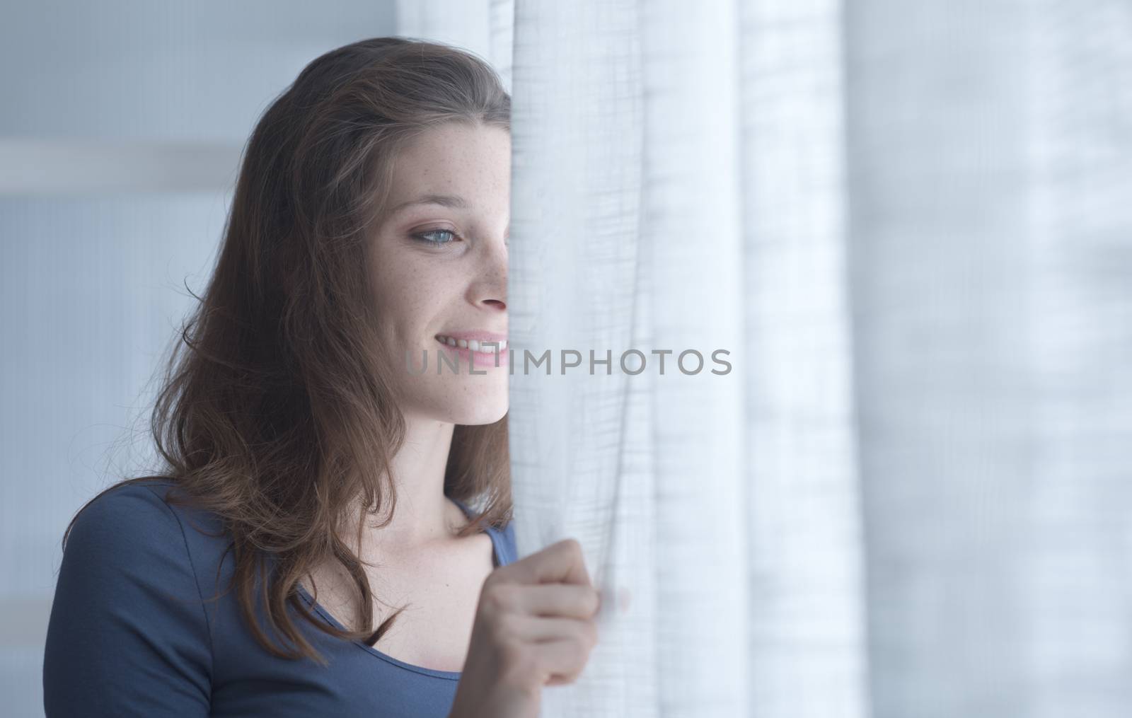 A young woman looking through her window early in the morning 
