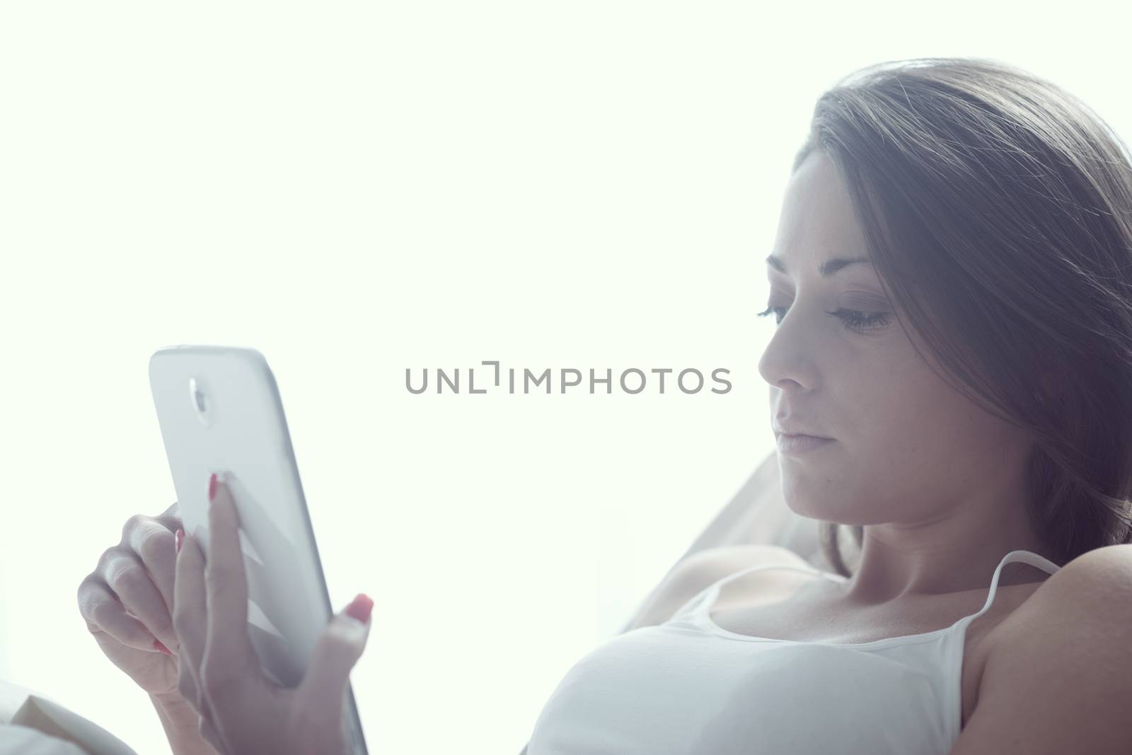 An attractive young female lying on her bed using a tablet 