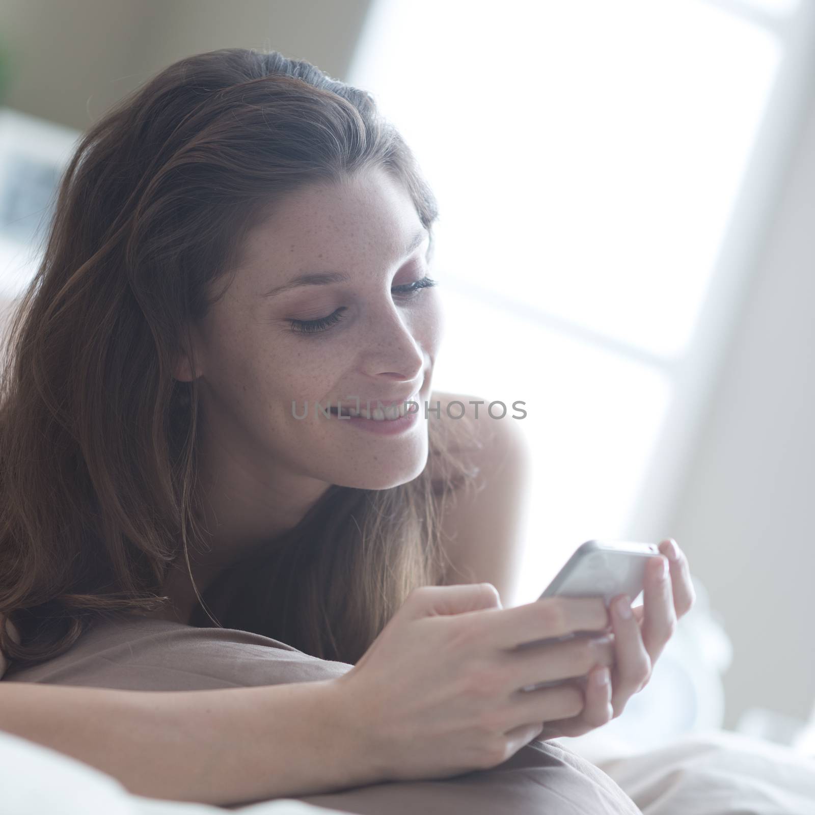 Relaxed woman at home reading a text message in her bright bedroom 