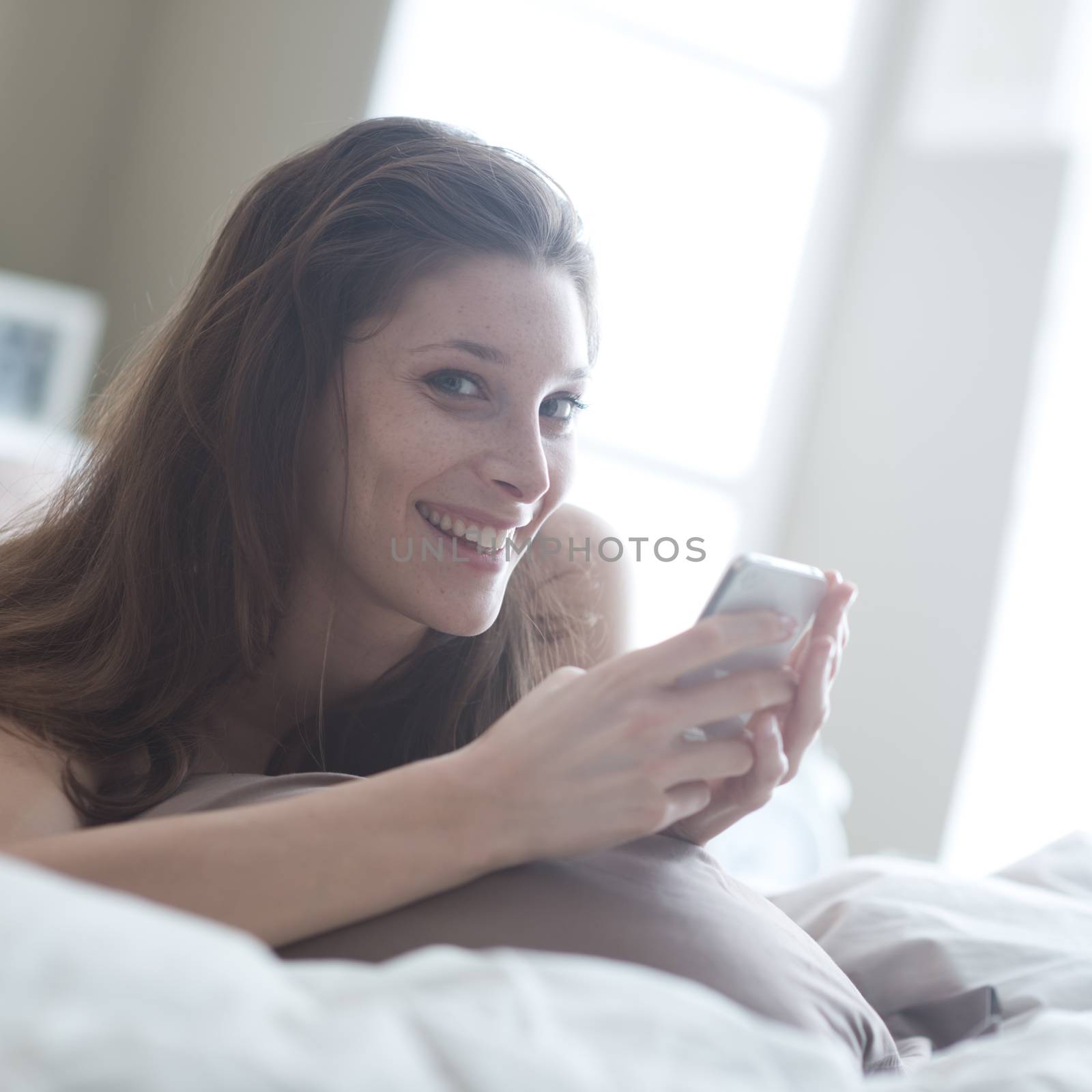 Relaxed woman at home reading a text message in her bright bedroom 