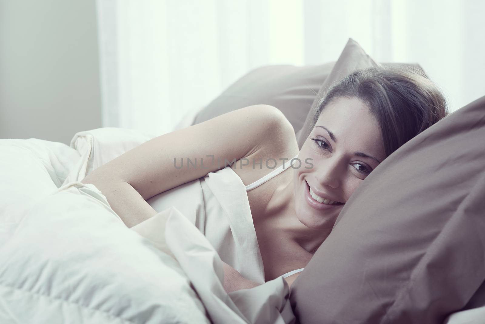 Young woman lying in bed and smiling at the camera 