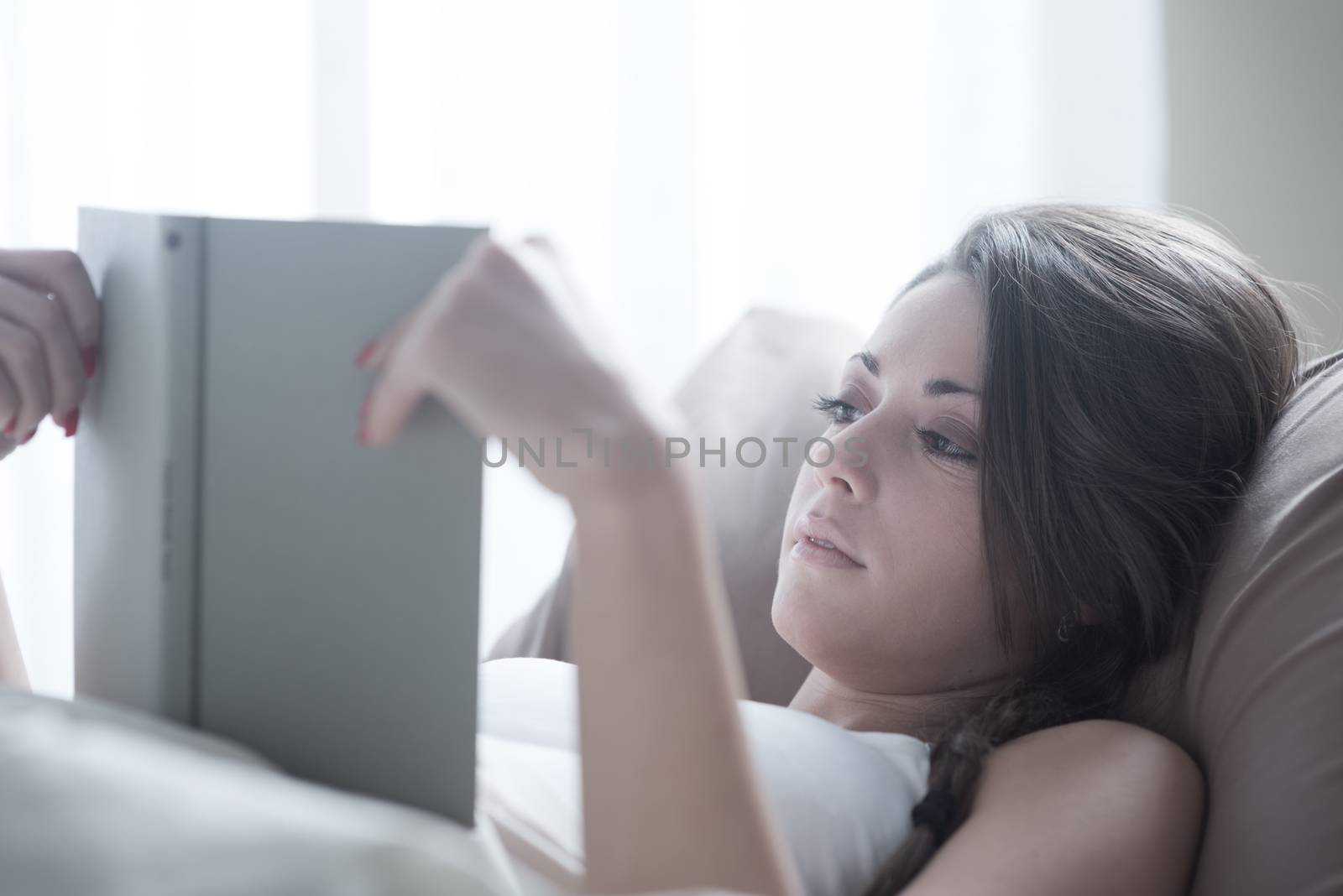 Woman lying in bed while reading a book 