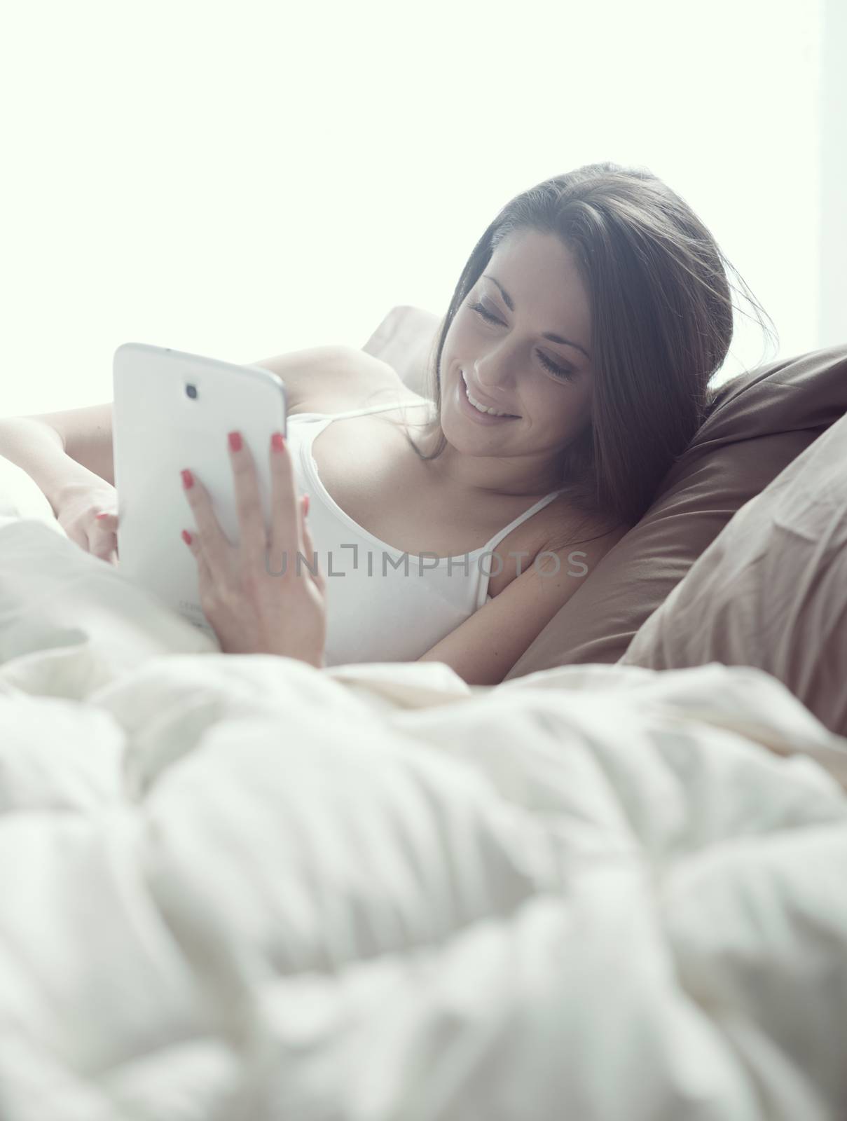 Woman enjoying with a digital tablet in bed in the morning, waking up.