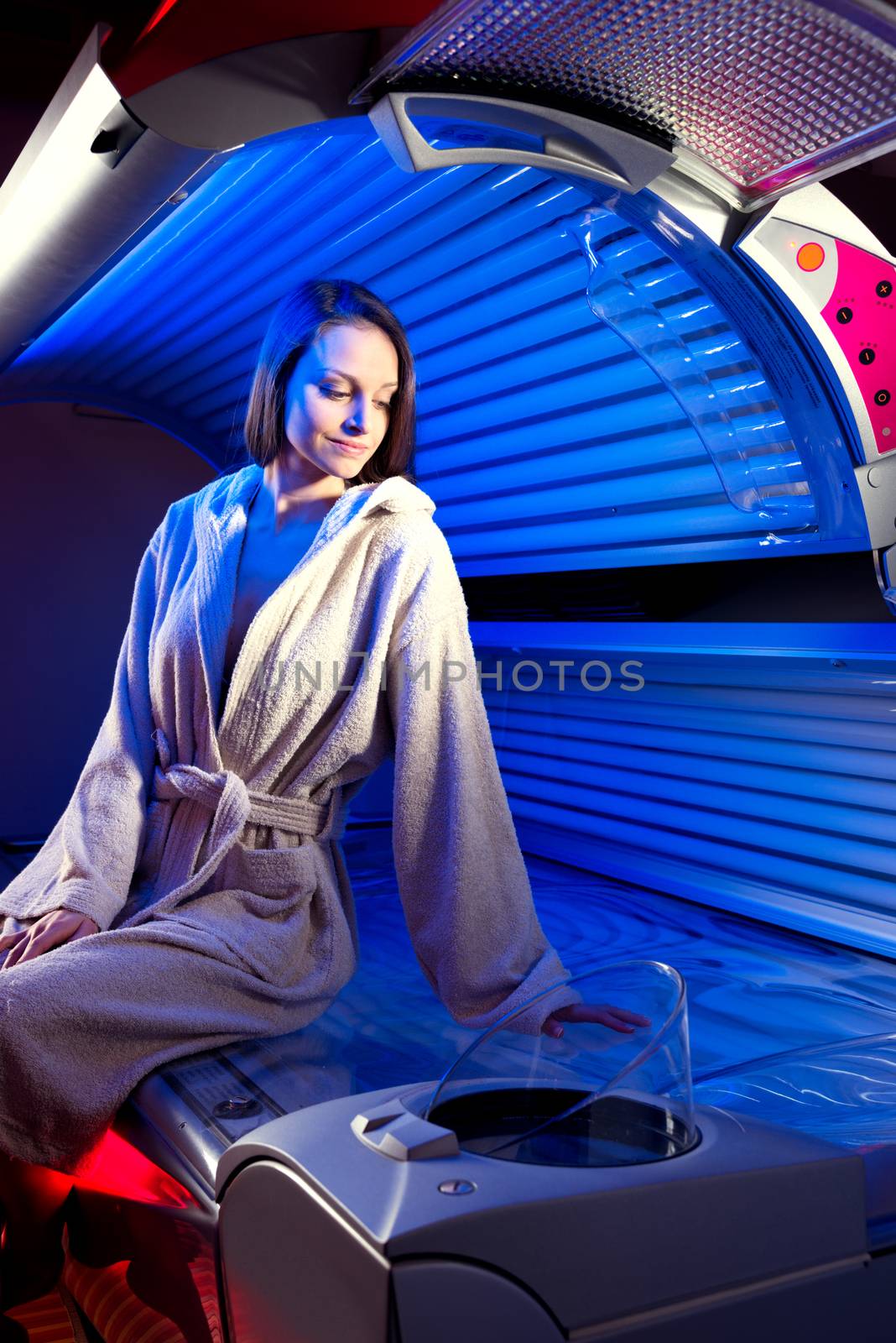 Young attractive woman wearing bathrobe and sitting on tanning bed.