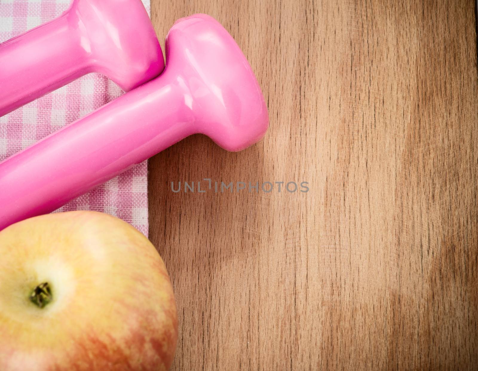 Fitness set Pink dumbells and apple on wooden table.Focus on the table 
