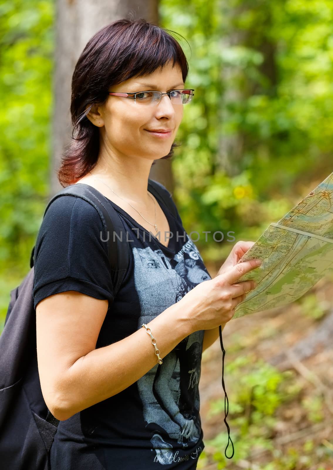 Woman smiling and sightseeing outdoors and holding a map in forrest