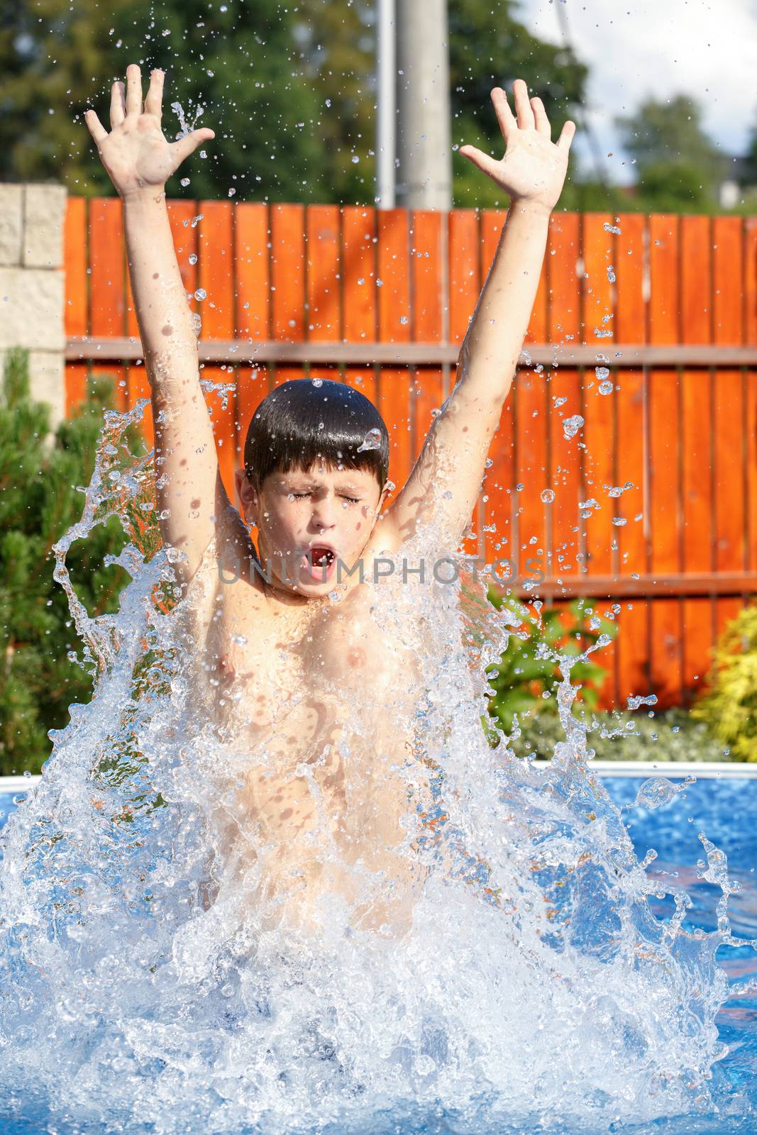 Boy jumping in the home garden swimming pool with clear water