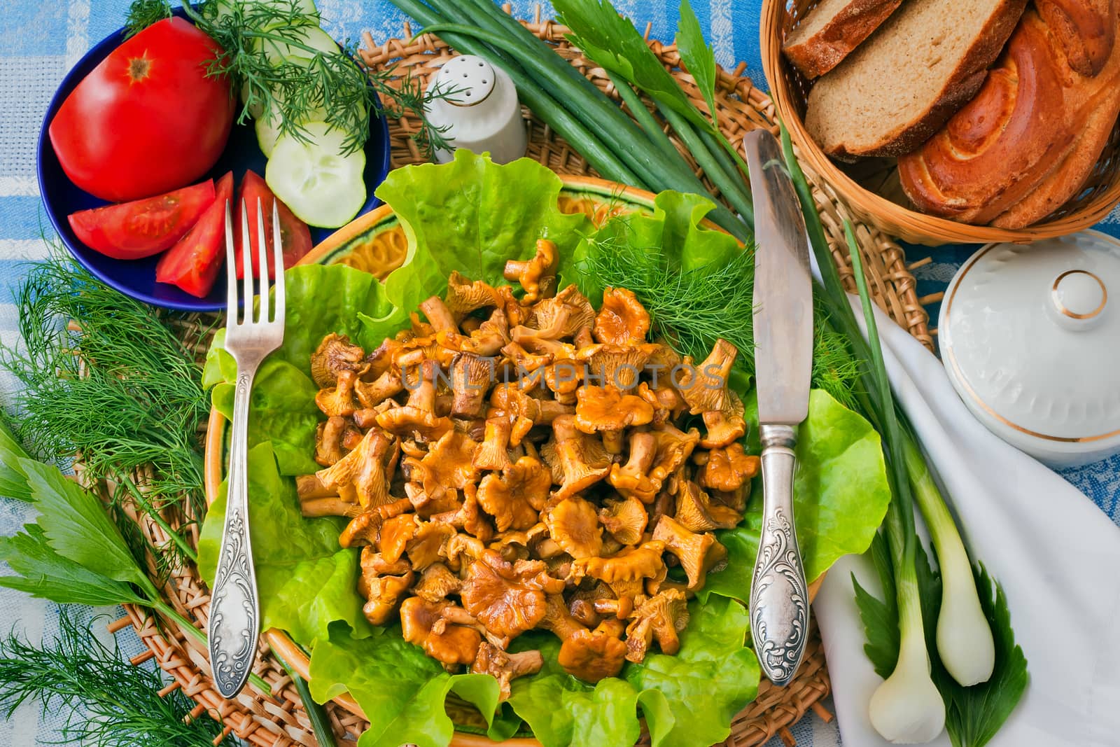 Dish with lettuce leaves on which appetizing fried chanterelles, and also vegetables, bread are located.