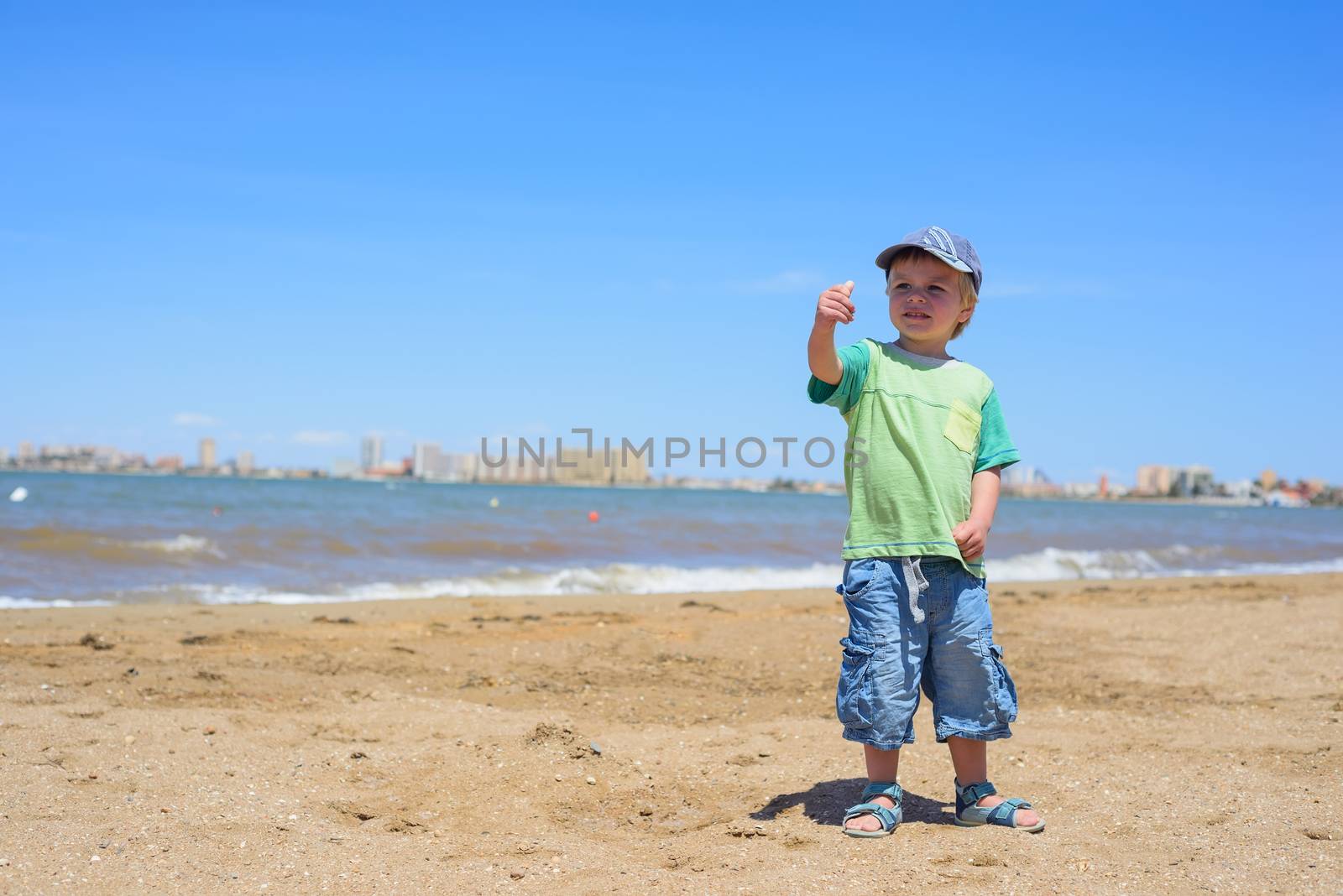 Happy boy pointing with his finger on sandy beach