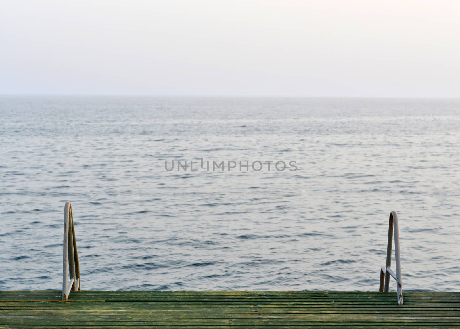 Wooden pier with metal handrails on the background of sea and sky