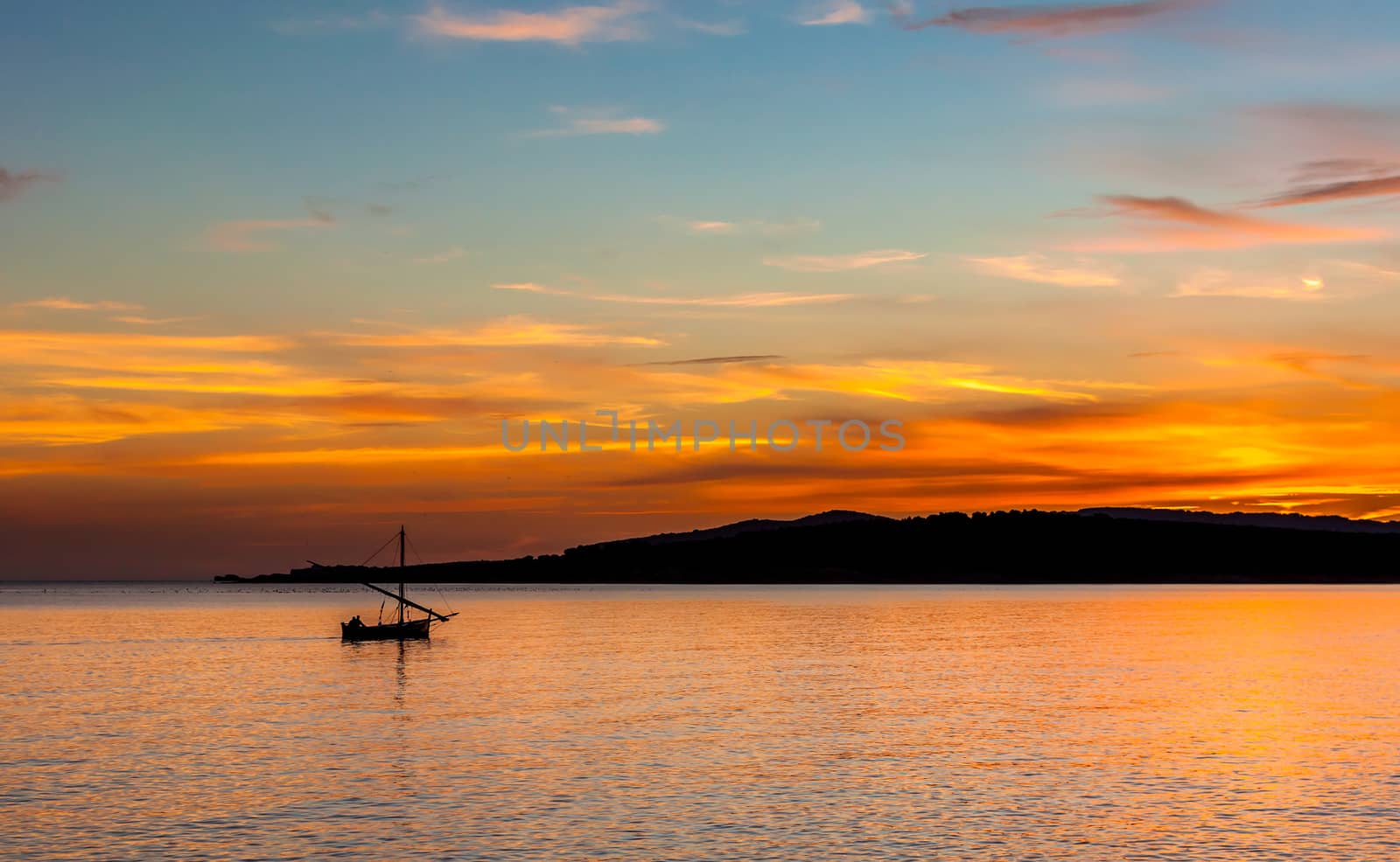 fishing boat on the coast at sunset in sardinia with a multicolor sky