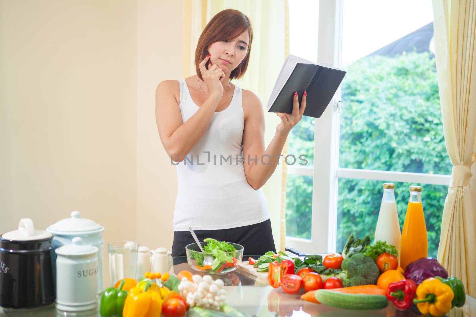 Young asian woman reads cookbook for recipe at kitchen