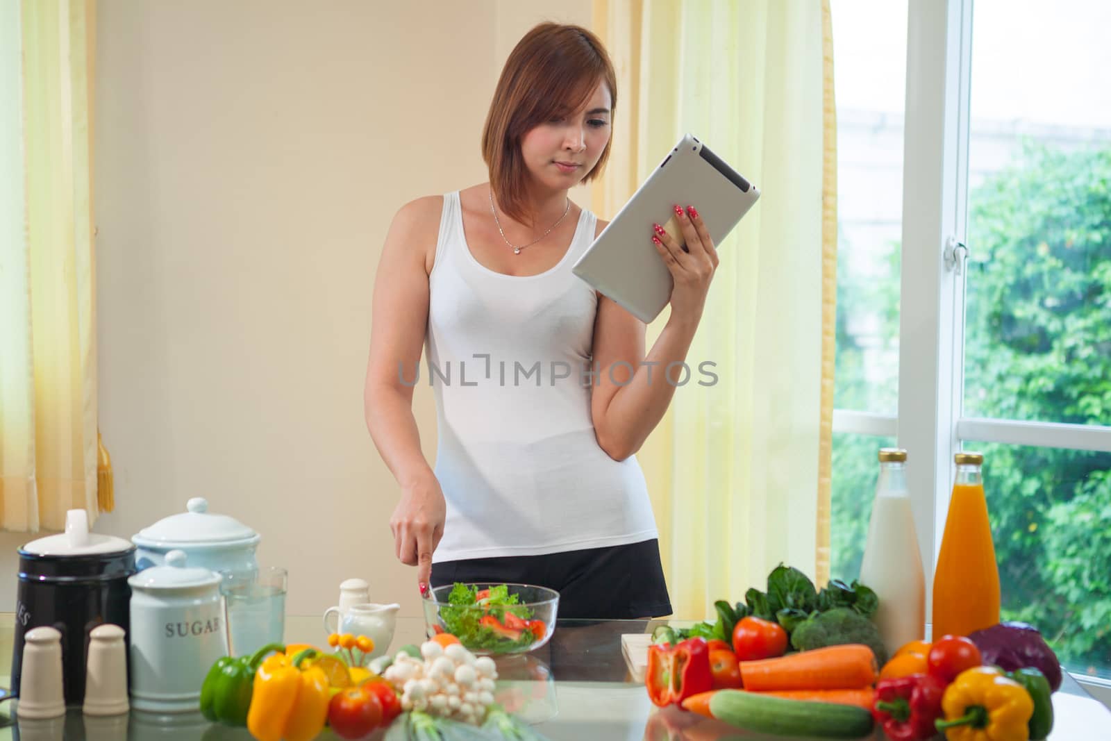 Young asian woman In Kitchen Following Recipe On Digital Tablet