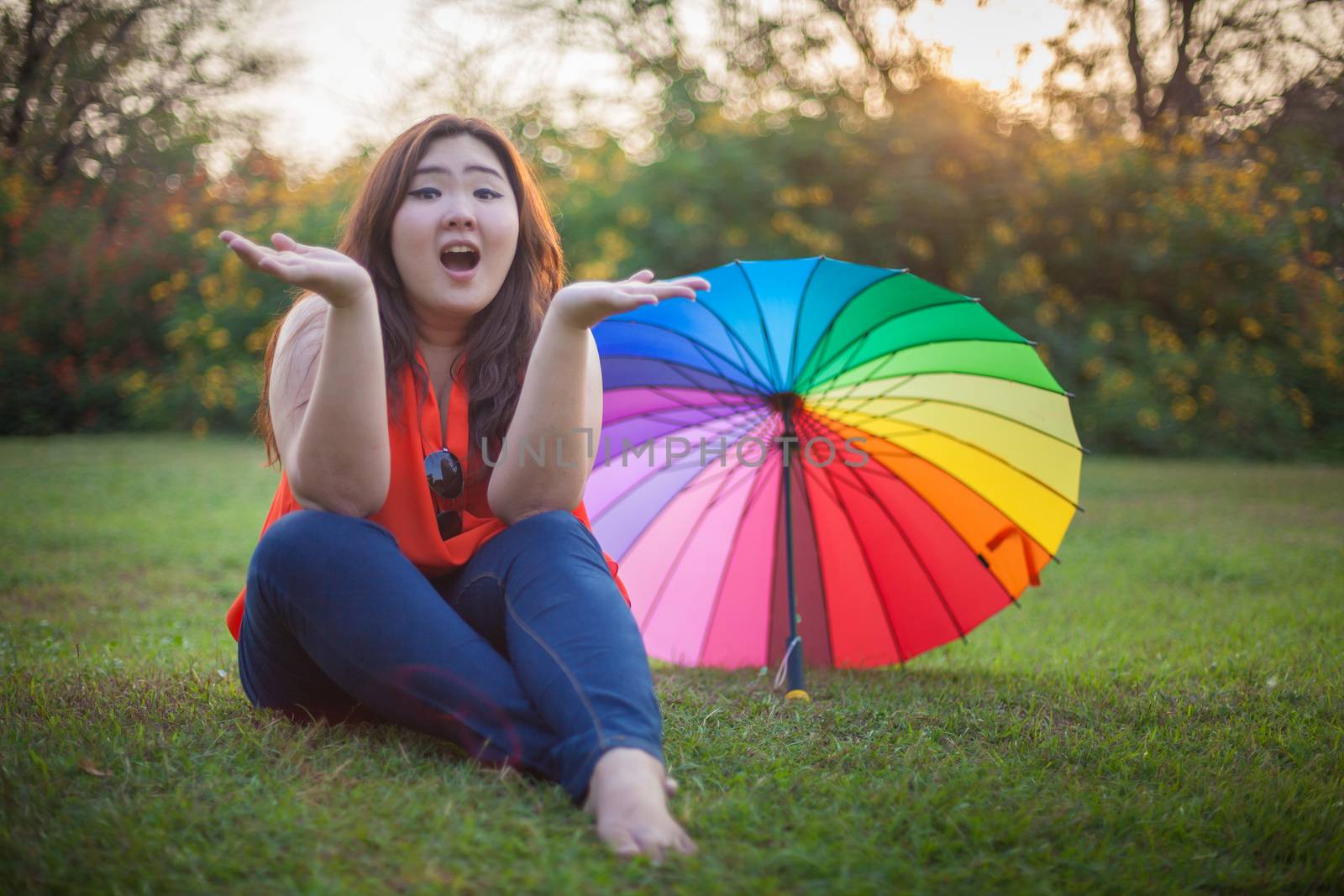 Young asian fat woman sitting with umbrella in autumn park