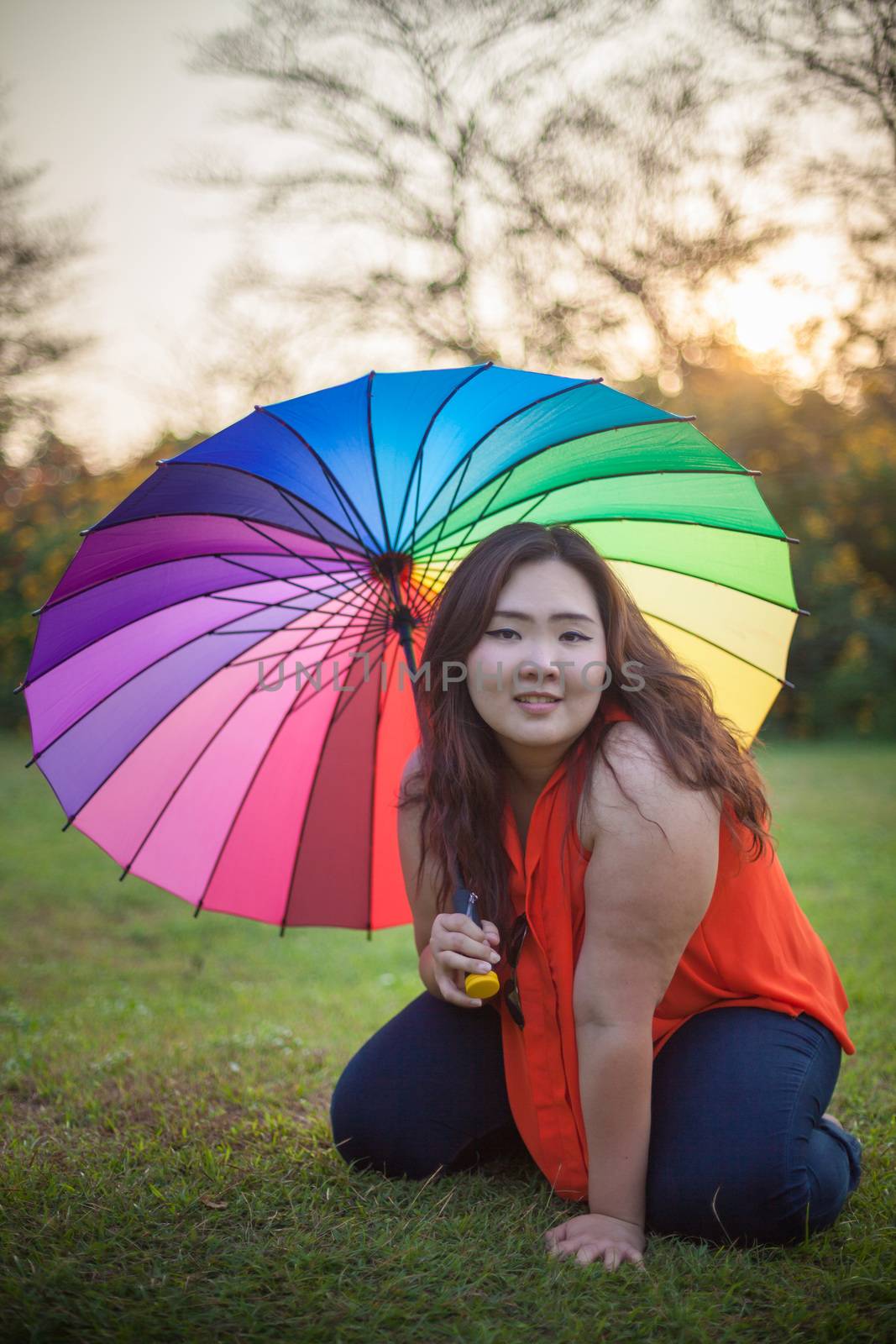 Young asian fat woman sitting with umbrella in autumn park