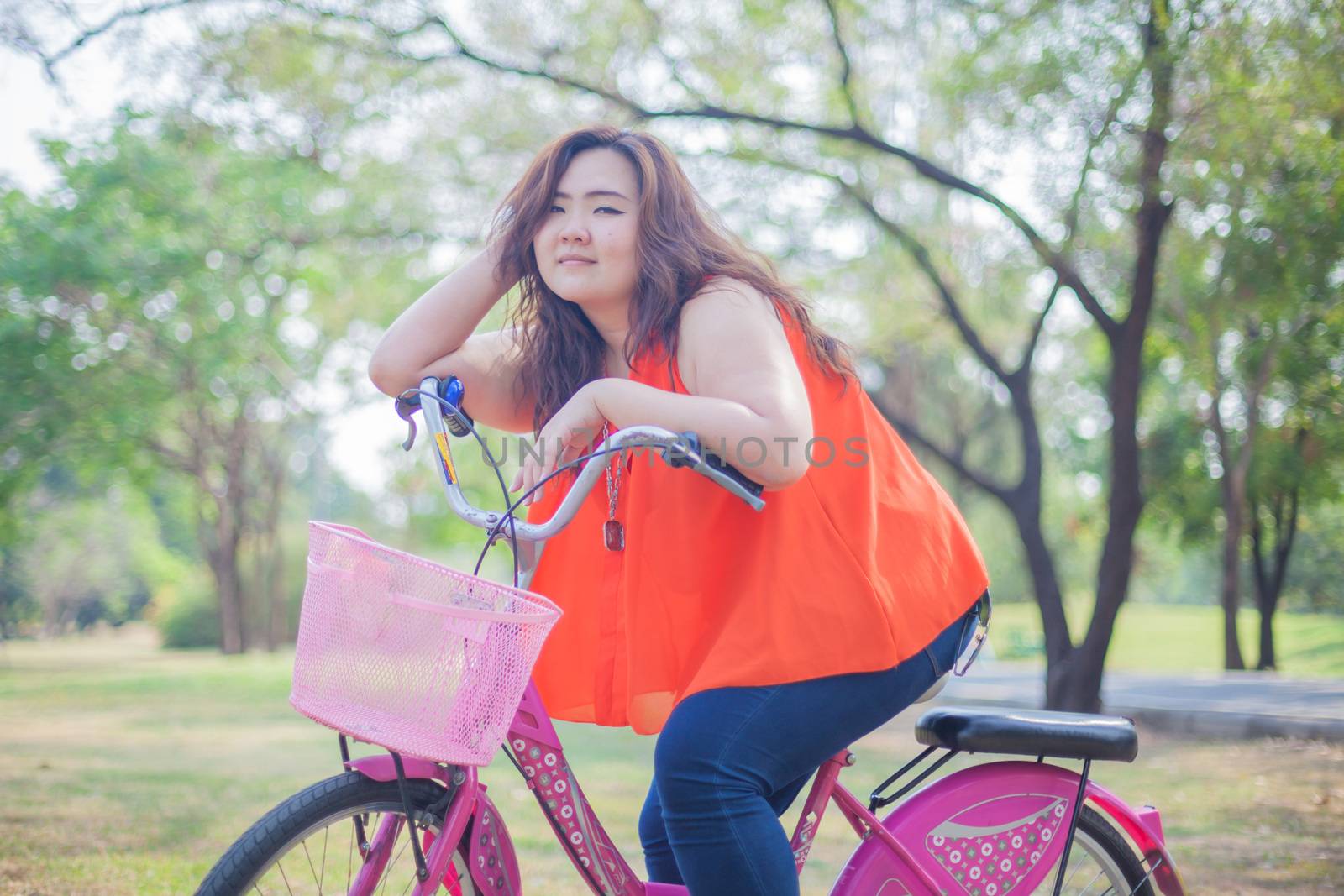 Happy fatty asian woman posing with bicycle outdoor in a park