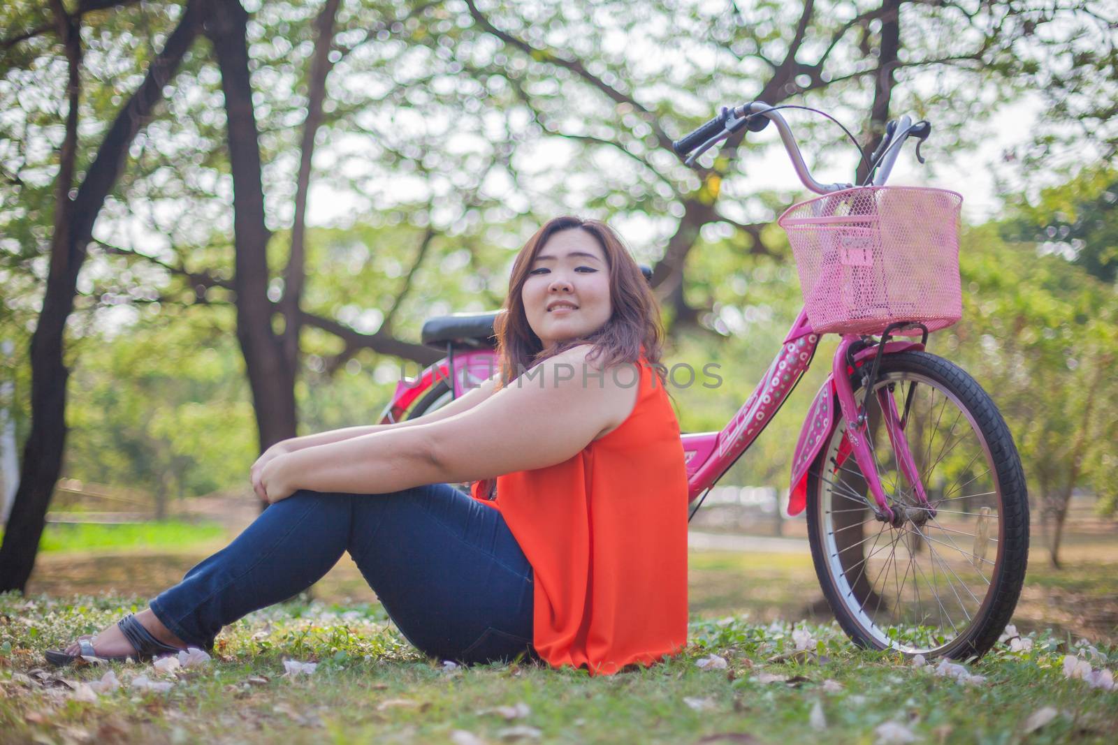 Happy fatty asian woman posing with bicycle outdoor in a park