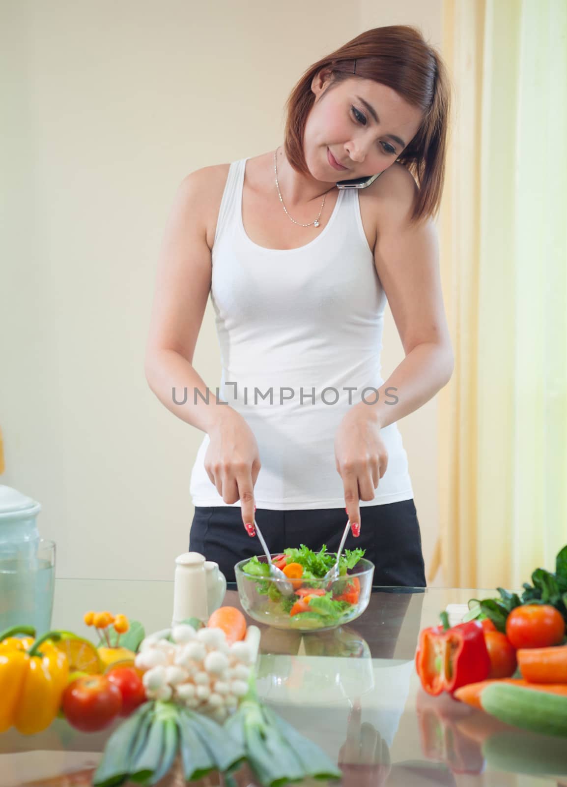 Young asian woman in kitchen and talking on the mobile phone by witthaya