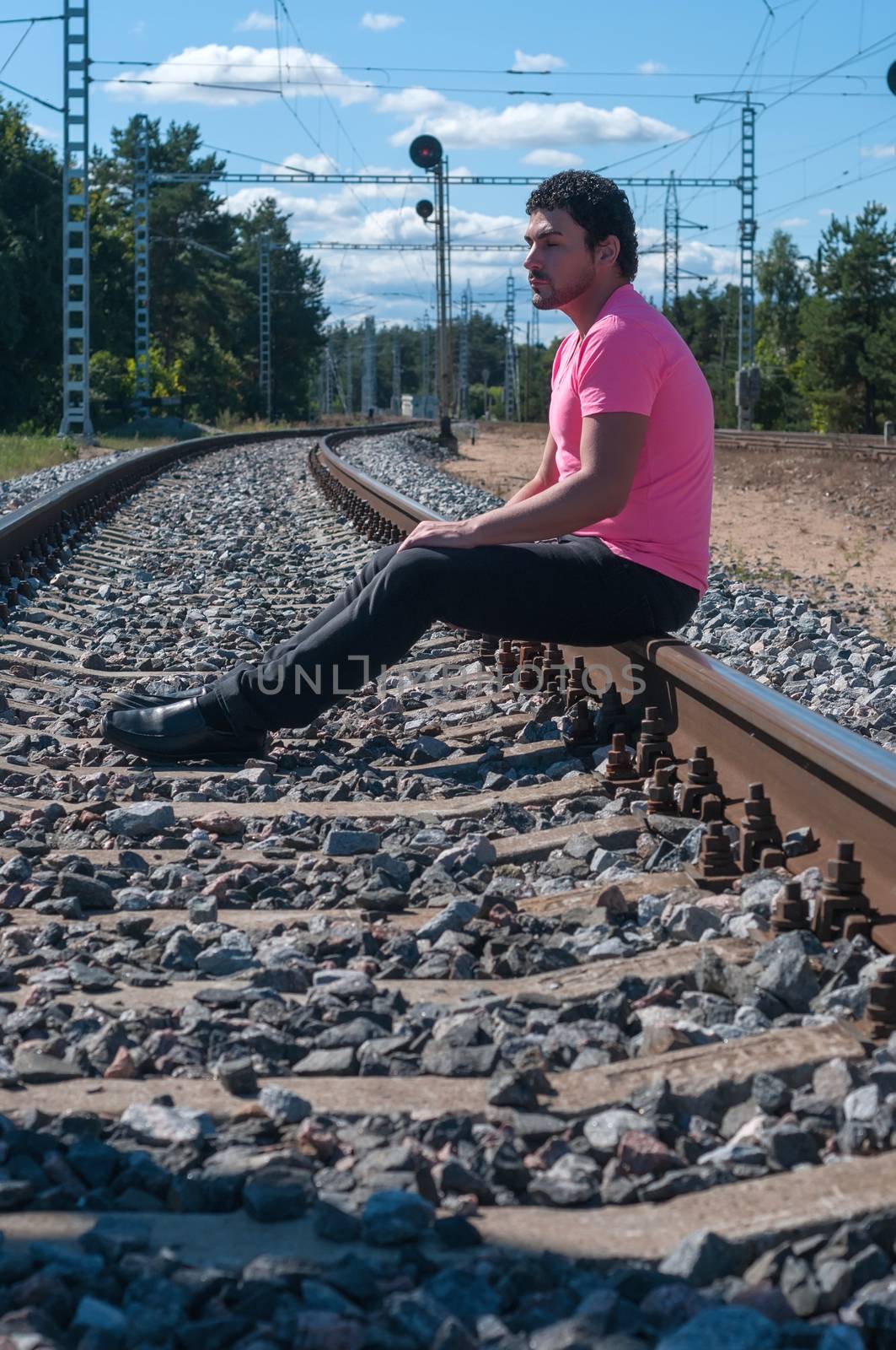 Shot of single man in pink t-shirt sitting on train tracks