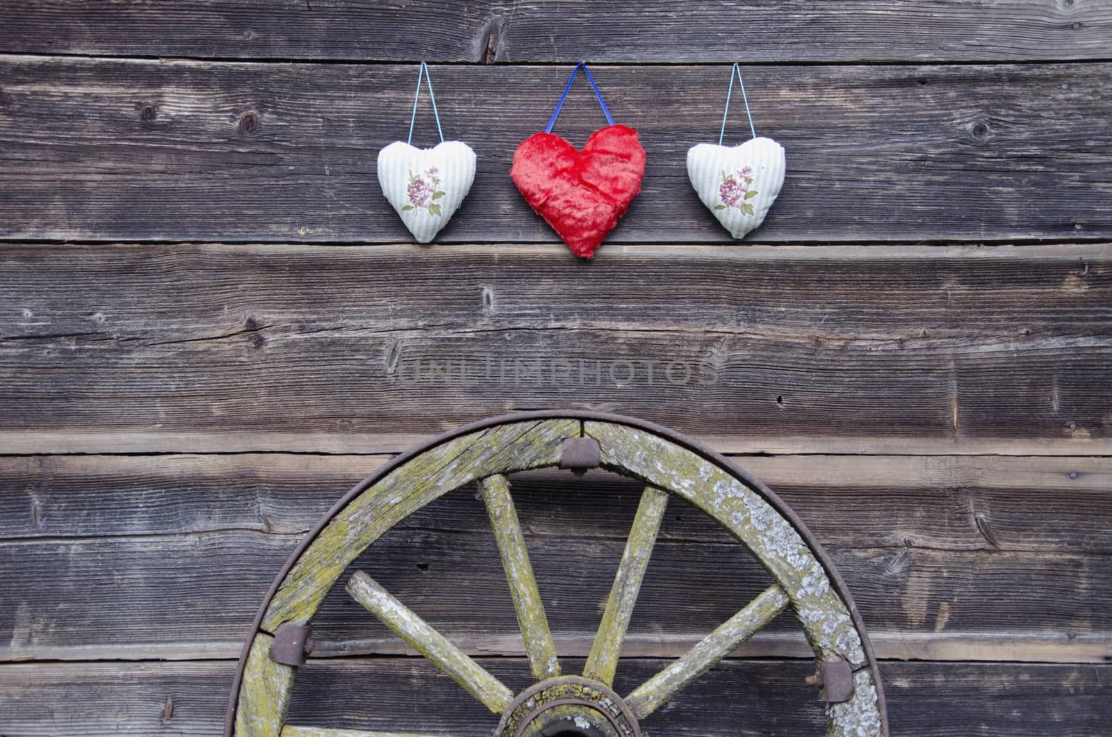 old barn wooden wall with three hearts and ancient carriage wheel
