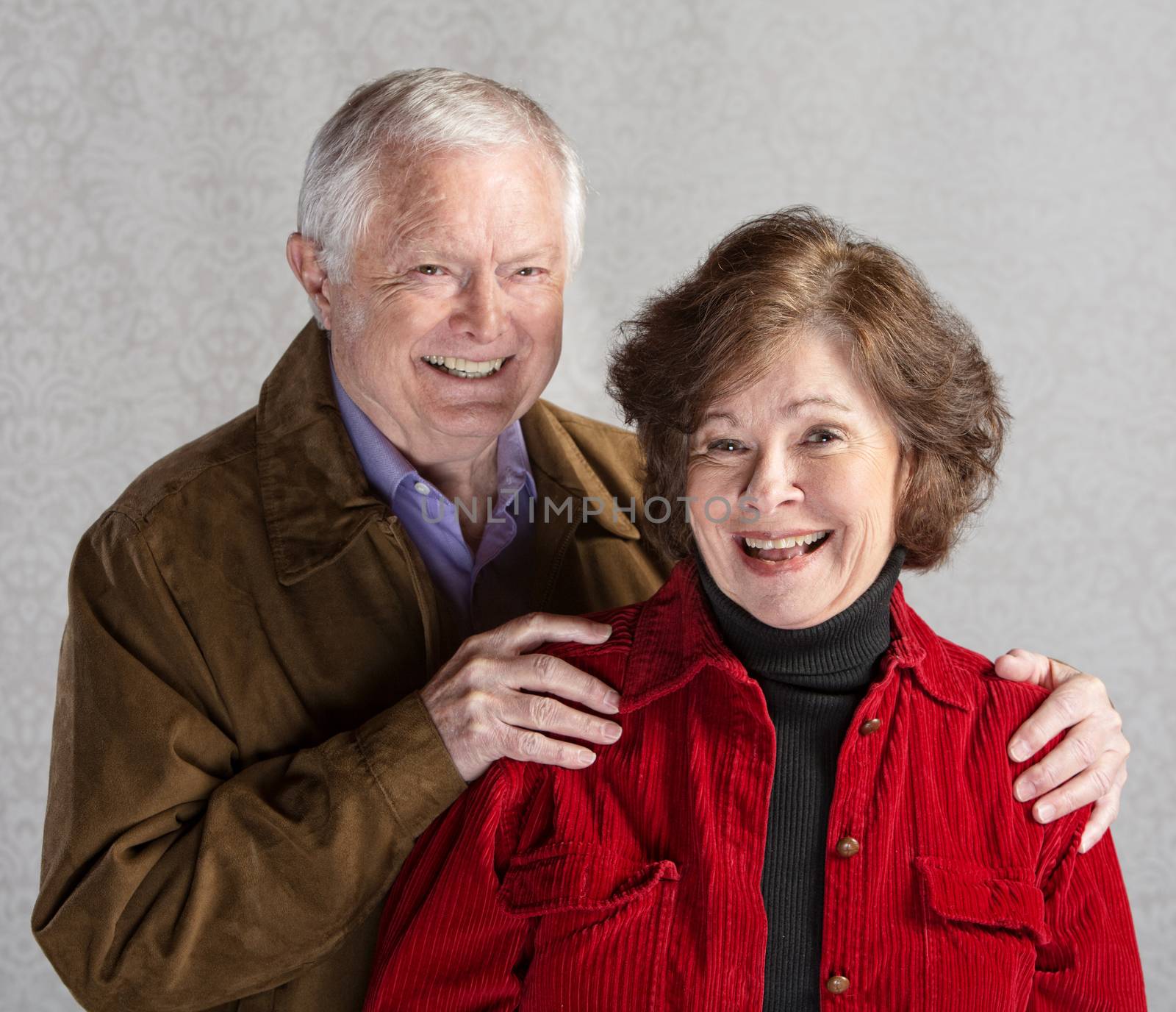 Elderly Caucasian couple laughing in front of gray background