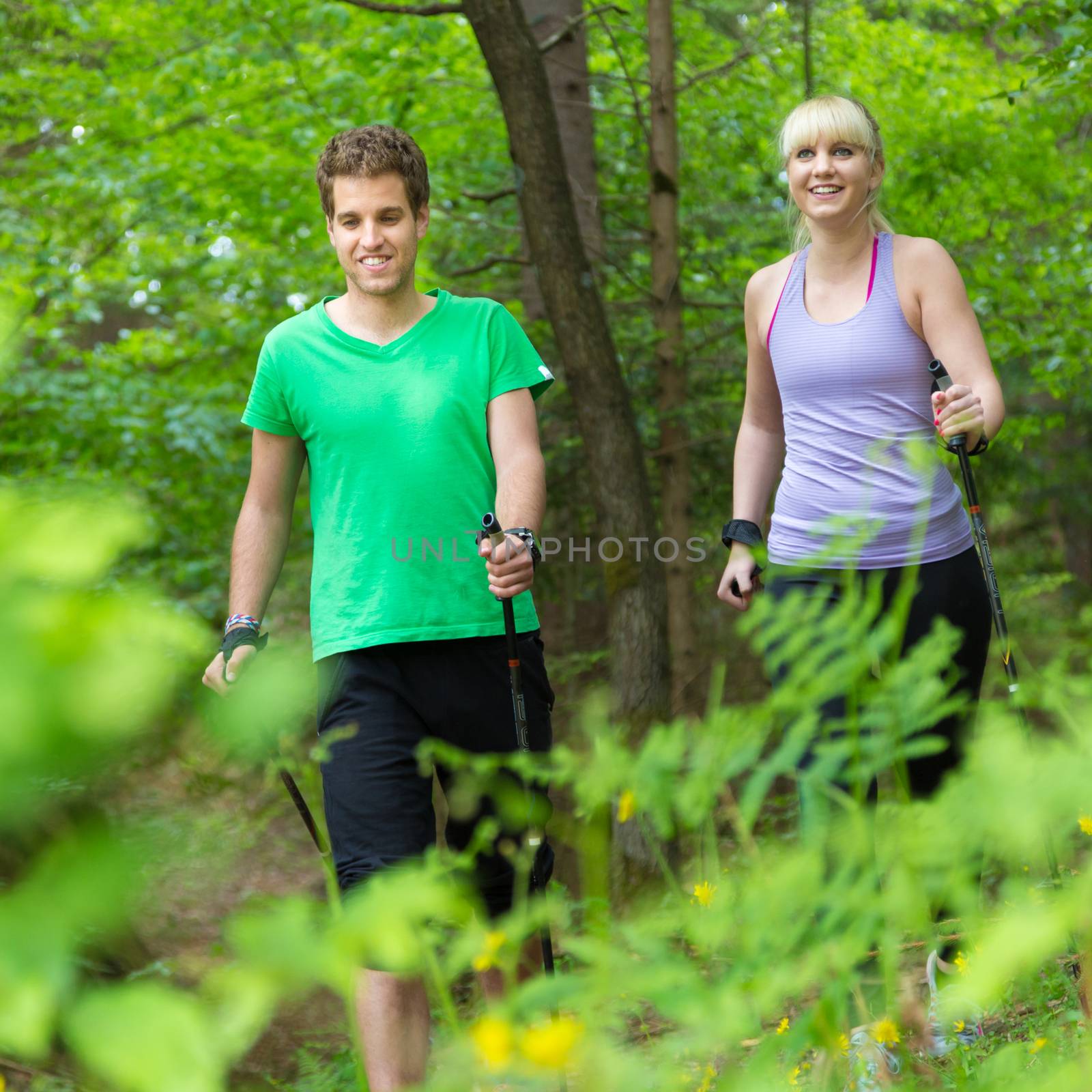 Young spoty active cople with hiking sticks walking in nature. Active lifestyle. Activities and recreation outdoors.