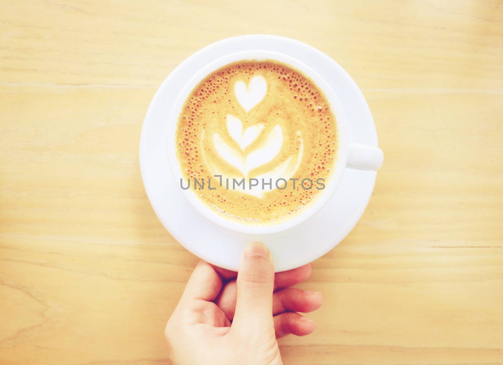 Hand holding cup of latte or cappuccino coffee with retro filter by nuchylee