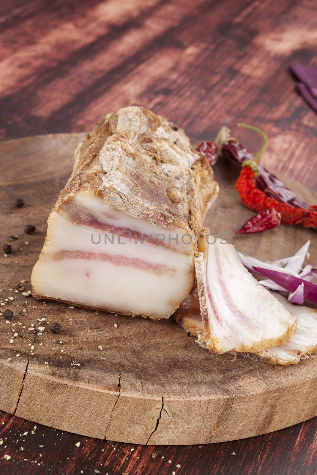 Big bacon piece and slices on wooden chopping board on wooden background. Traditional meat eating. 