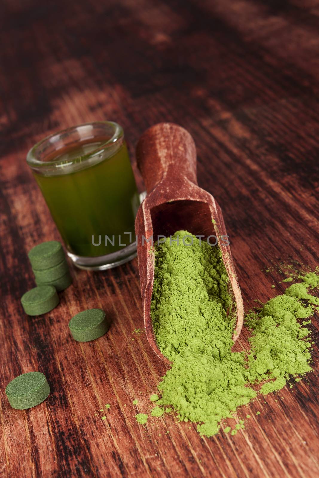 Nutritional supplements chlorella, spirulina and wheat grass on wooden background. Pills, green drink and ground powder. Green superfood. Alternative medicine and detox. 