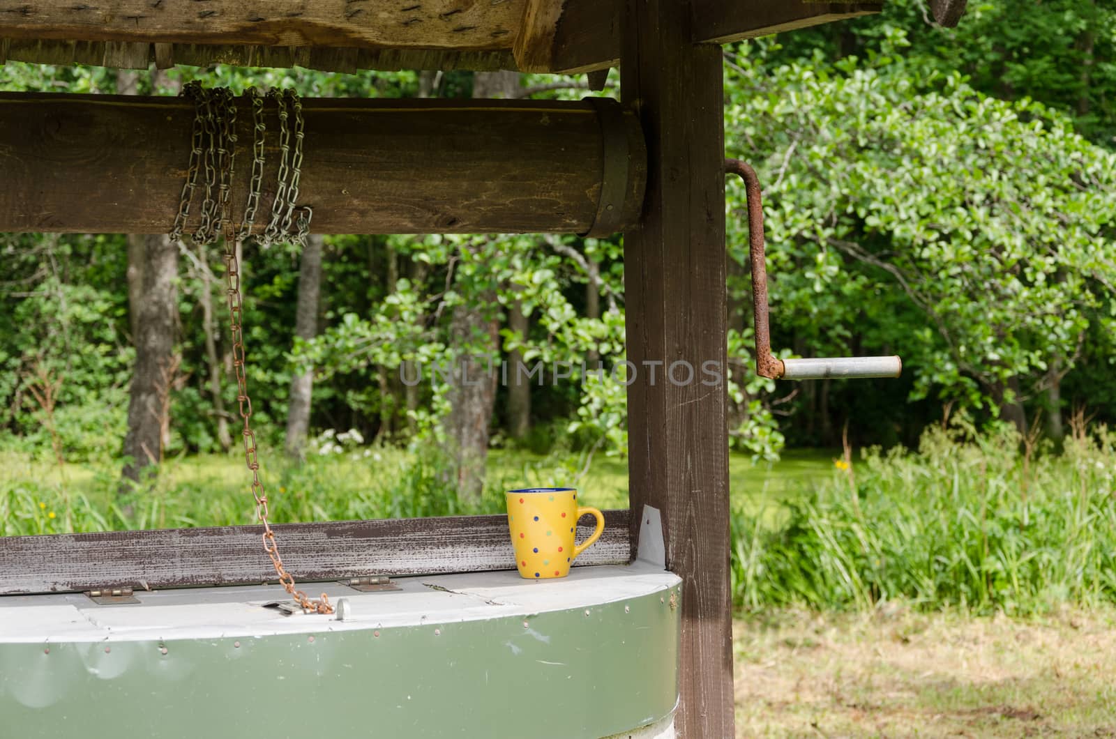 edge of old rustic well pulley with chain and mottled clay cup