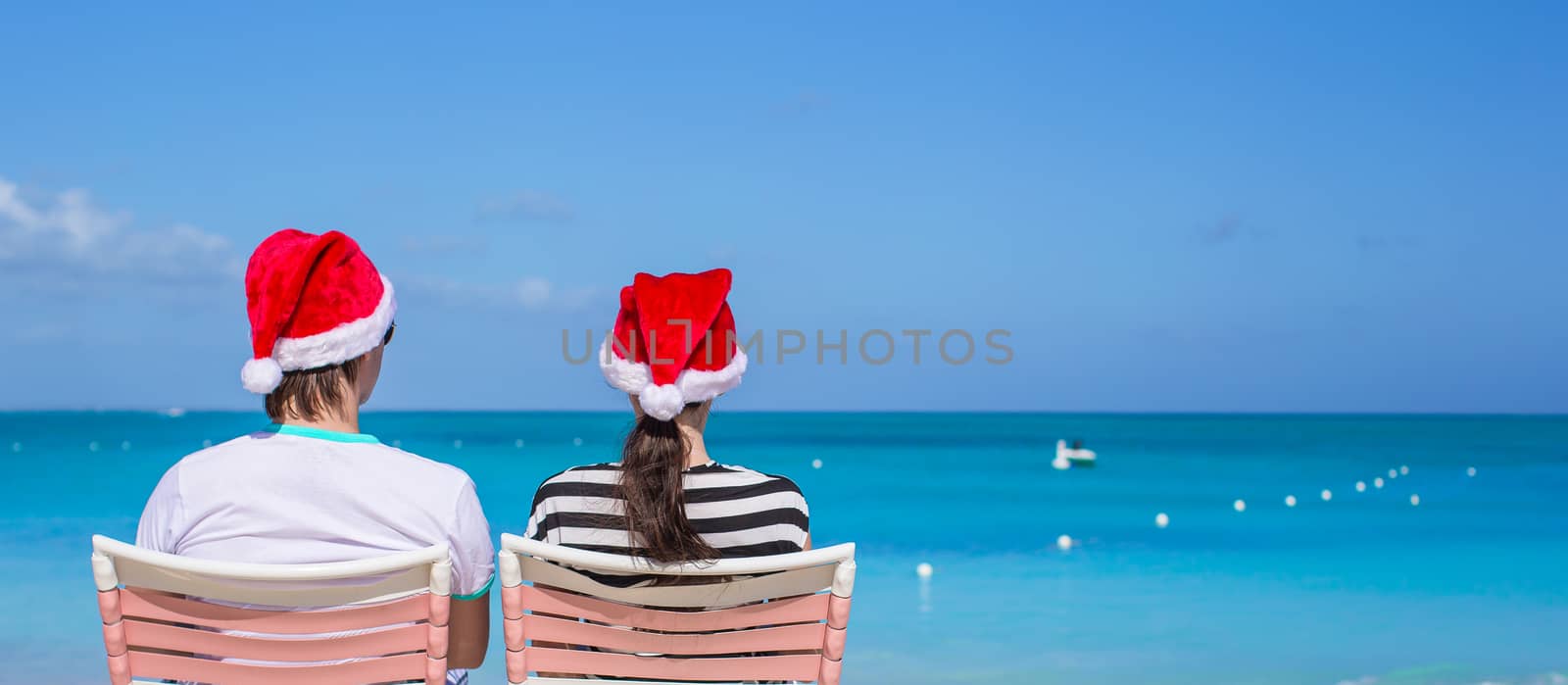 Back view of young couple in Santa hats enjoy beach vacation by travnikovstudio