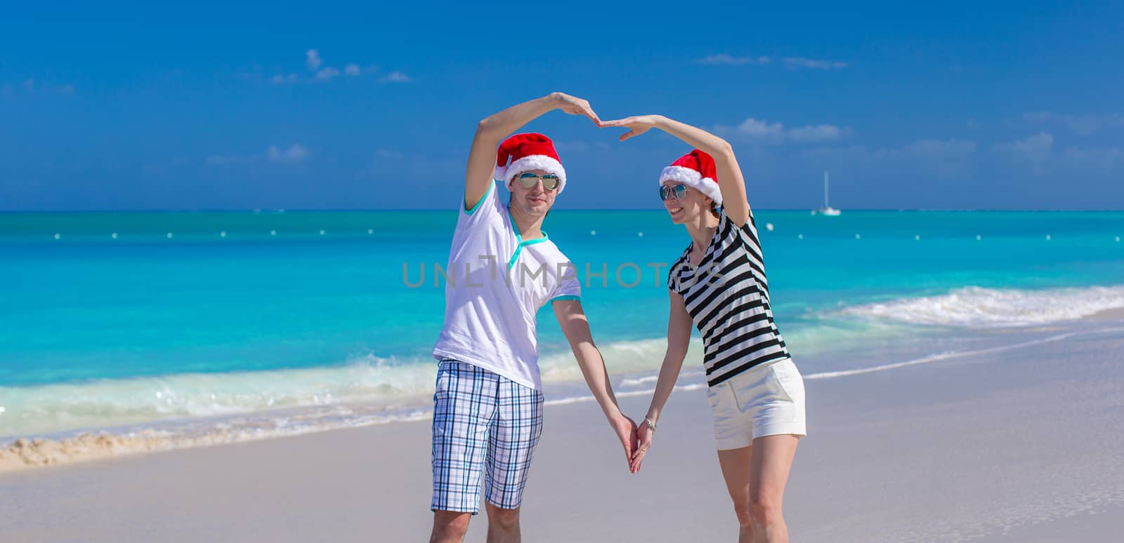 Portrait of young couple in Santa hats enjoy beach vacation by travnikovstudio