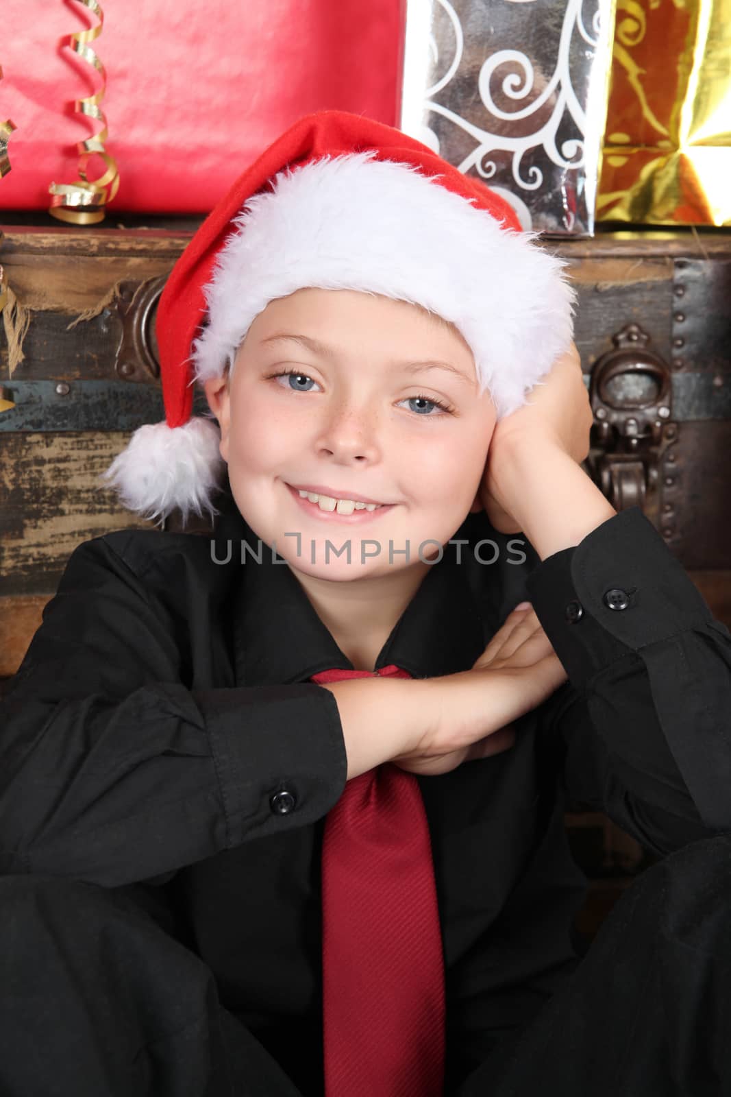 Young boy sitting against antique trunk surrounded by gifts