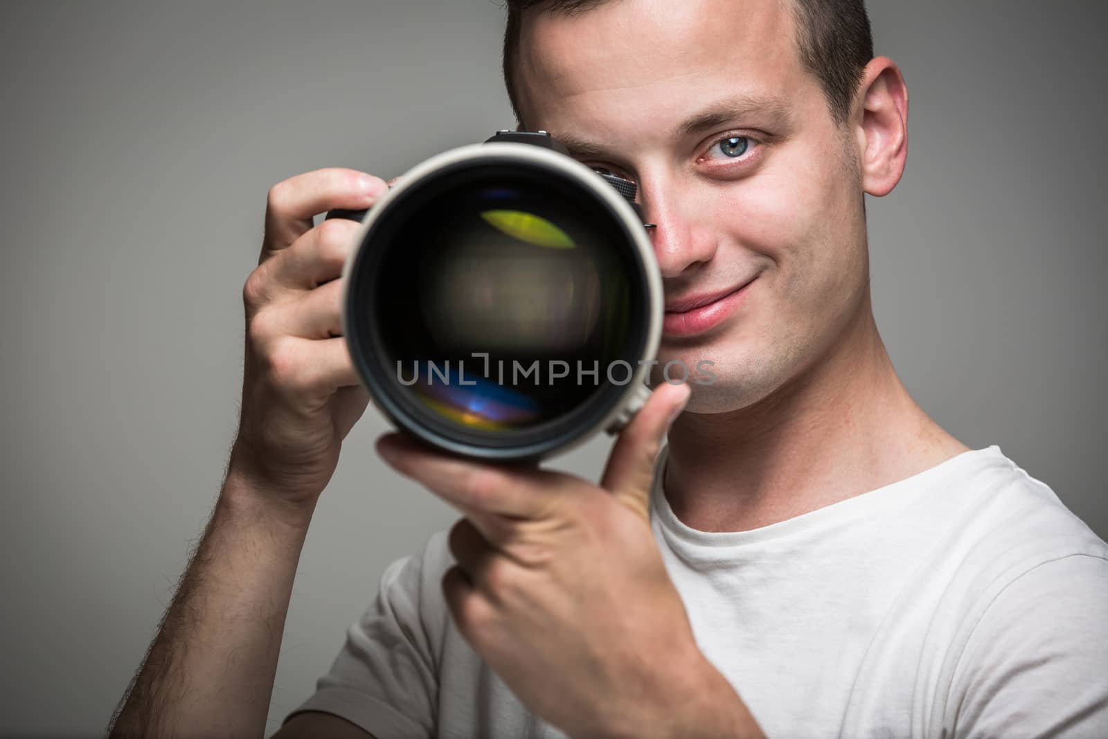 Young pro photographer with digital camera - DSLR and a huge telephoto lens in his well equiped studio, taking photos (color toned image; shallow DOF)