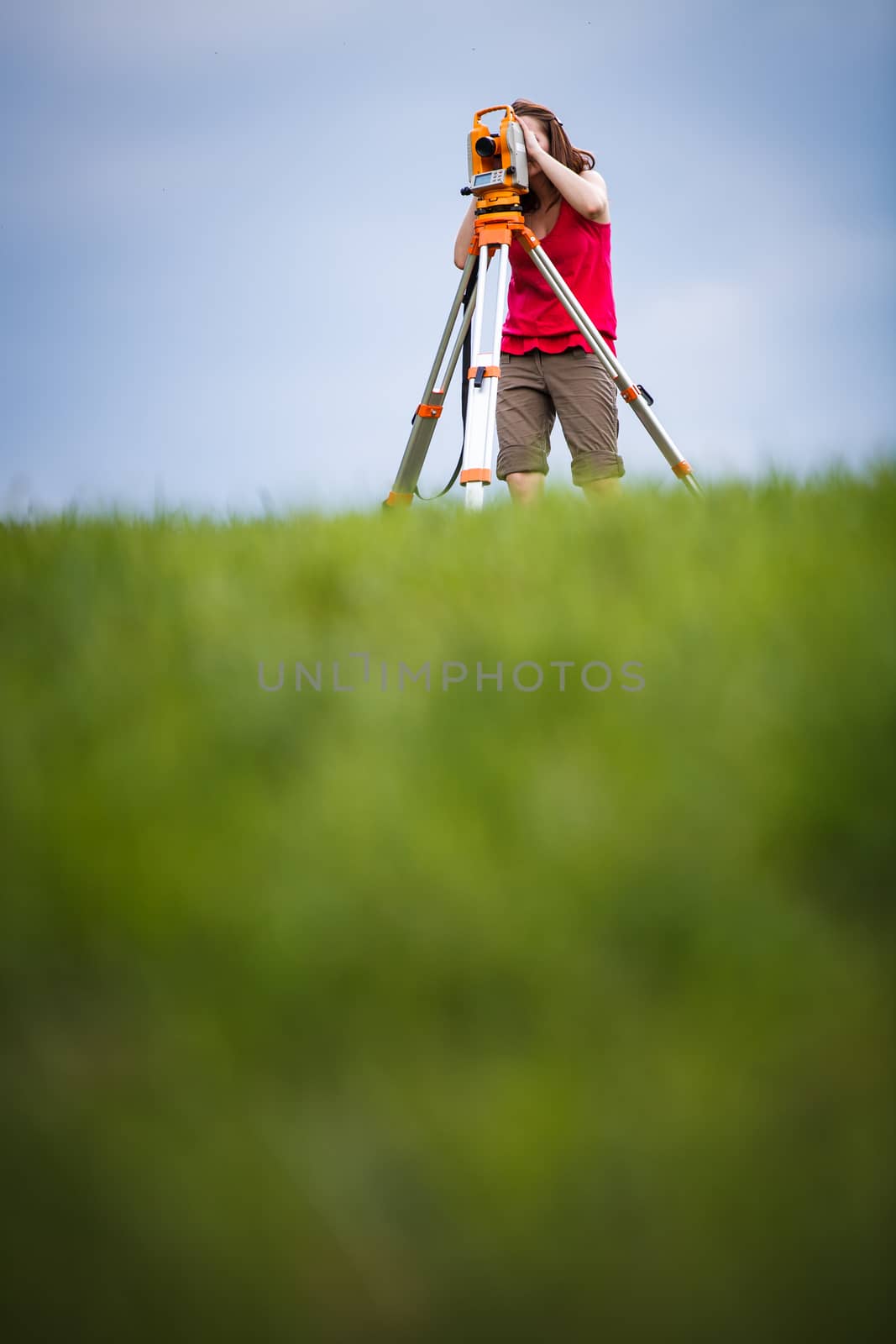 Young, female land surveyor at work - using the theodolite level outdoors