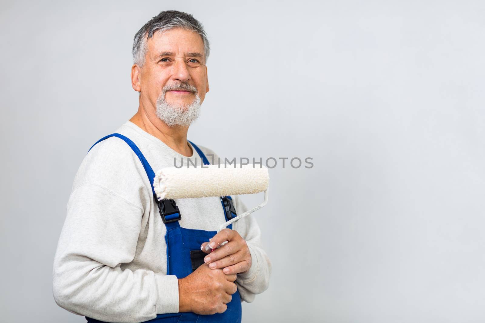 Senior man posing with a paint roller after having paint a white wall