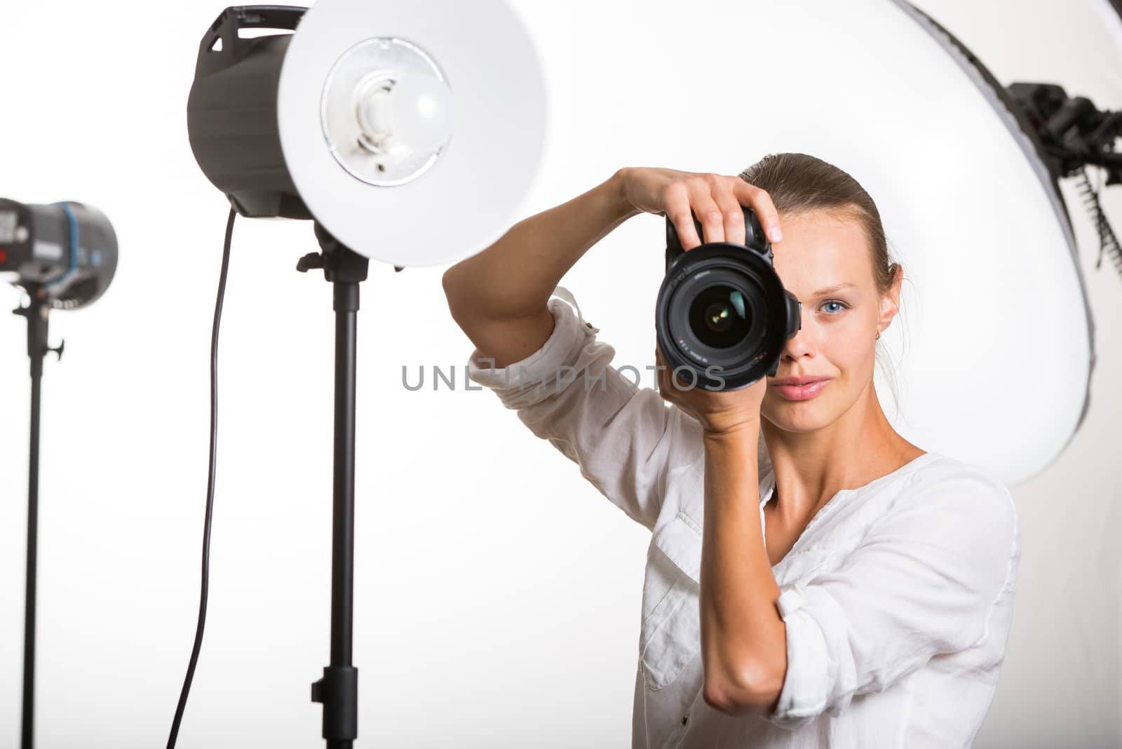 Pretty, female pro photographer with digital camera - DSLR and a huge telephoto lens in her well equiped studio, taking photos (color toned image; shallow DOF)