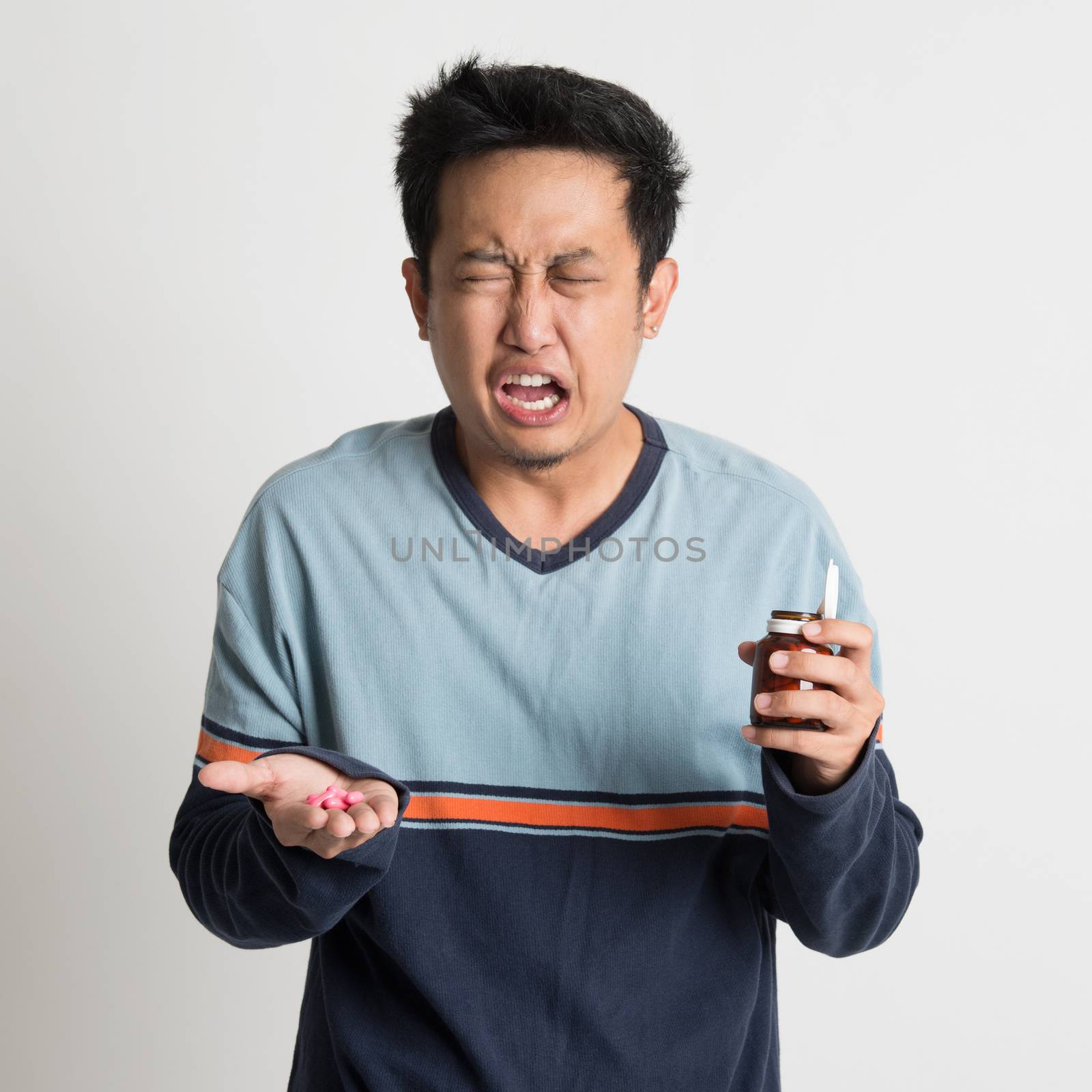 Asian male holding medicine bottle while sneezing, on plain background
