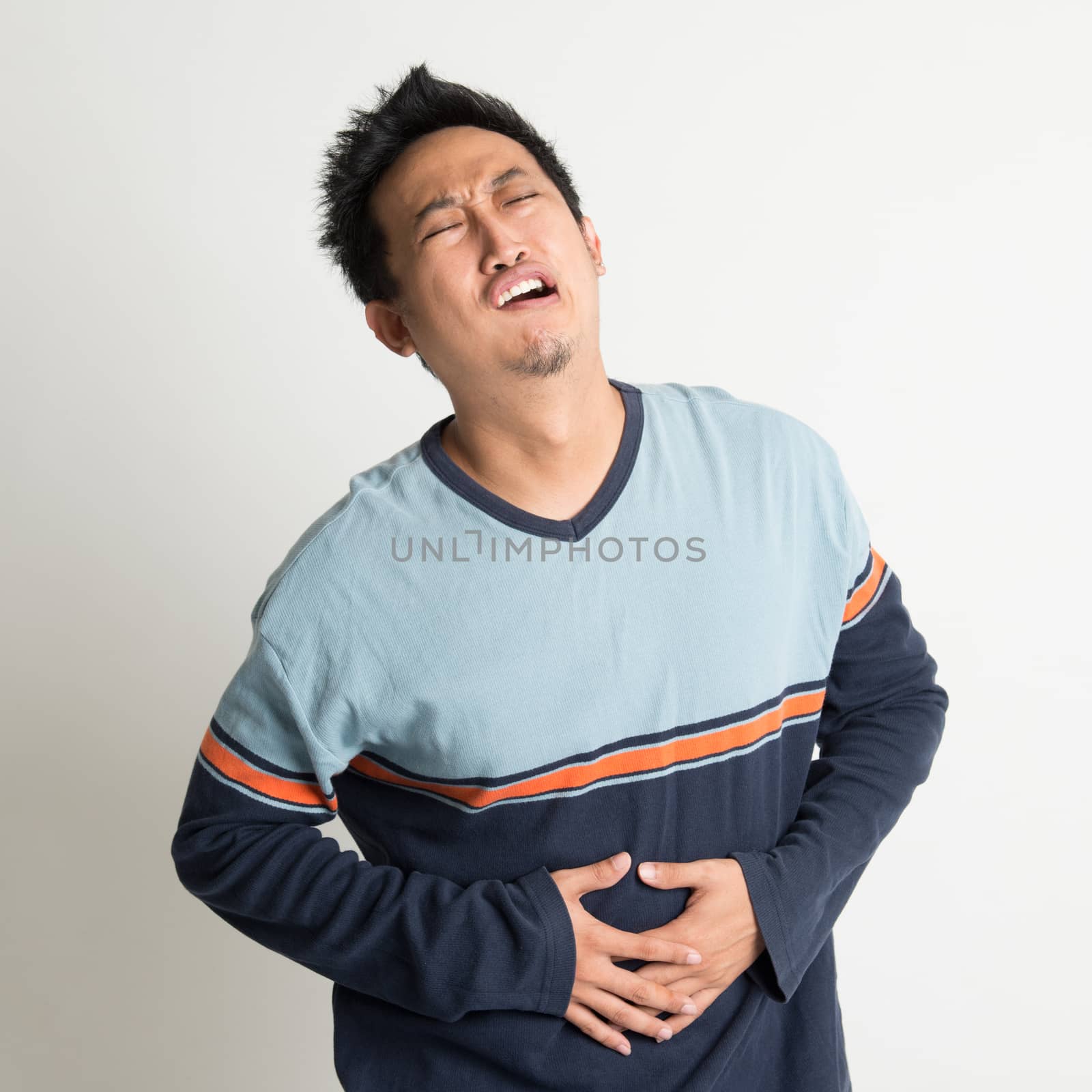 Asian male stomach pain, with painful face expression, on plain background