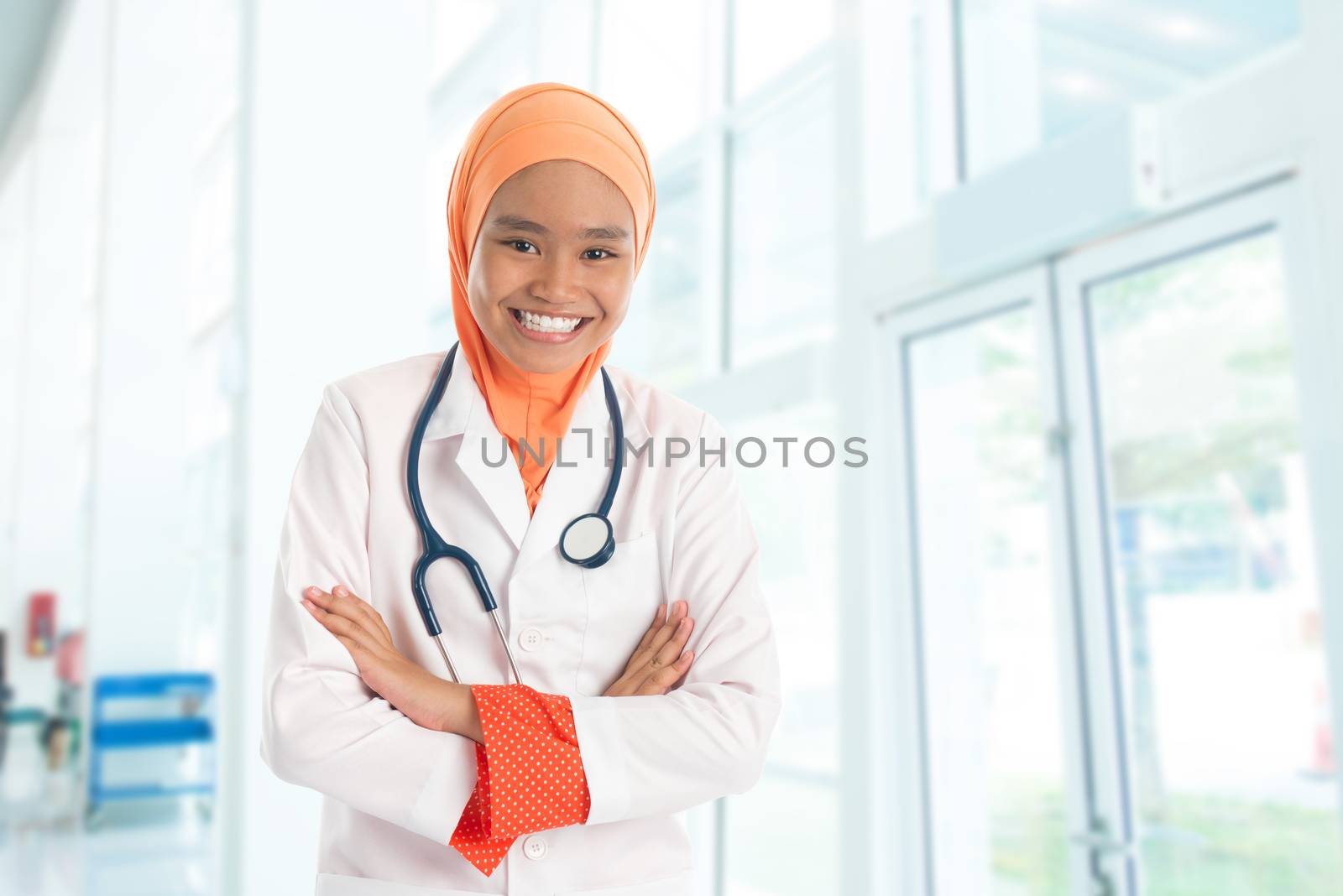 Cheerful young Muslim female doctor portrait, standing inside hospital