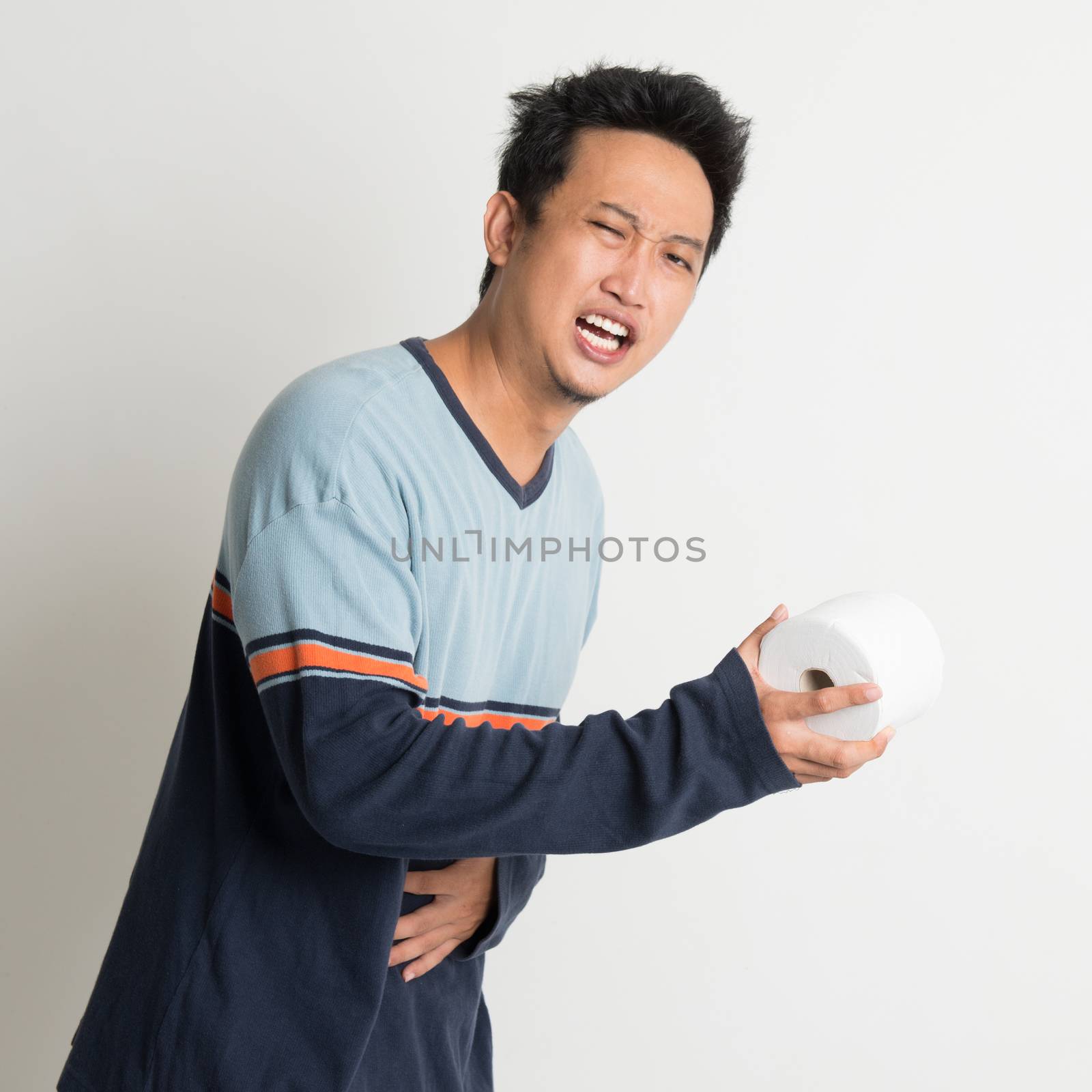 Asian male stomach pain holding toilet paper running to toilet, with painful face expression, on plain background
