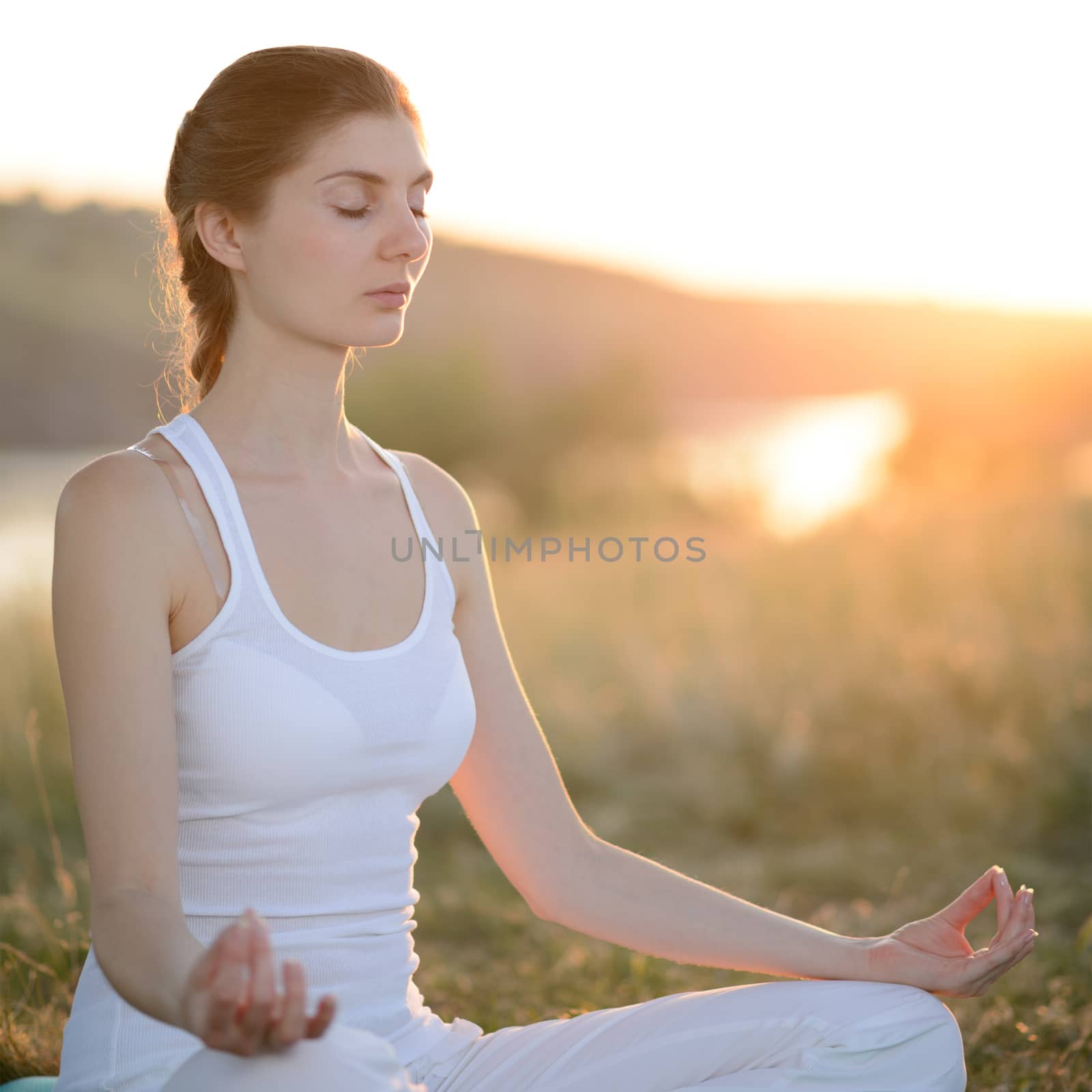 Young Beautiful Woman Practices Yoga on the Sunny Meadow by maxpro