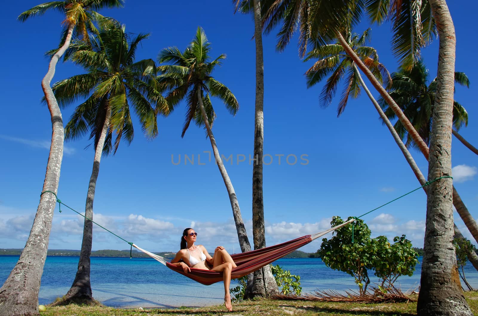 Young woman in bikini sitting in a hammock between palm trees, O by donya_nedomam