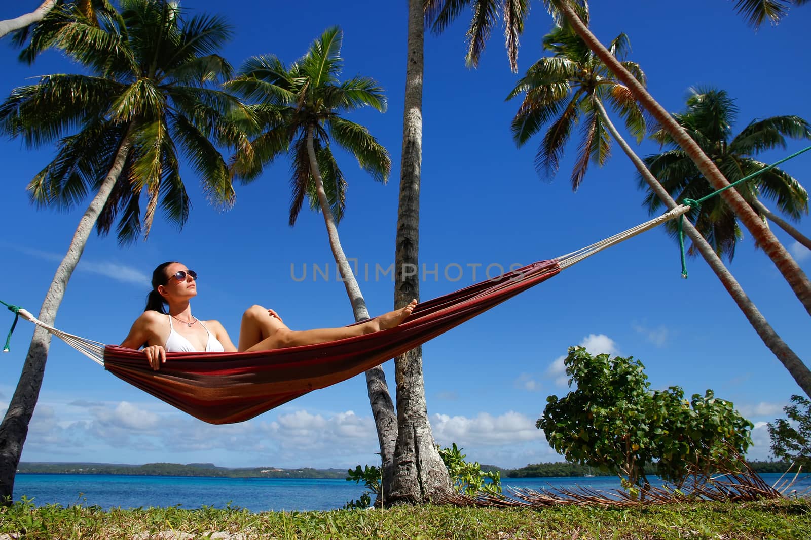 Young woman in bikini sitting in a hammock between palm trees, Ofu island, Vavau group, Tonga