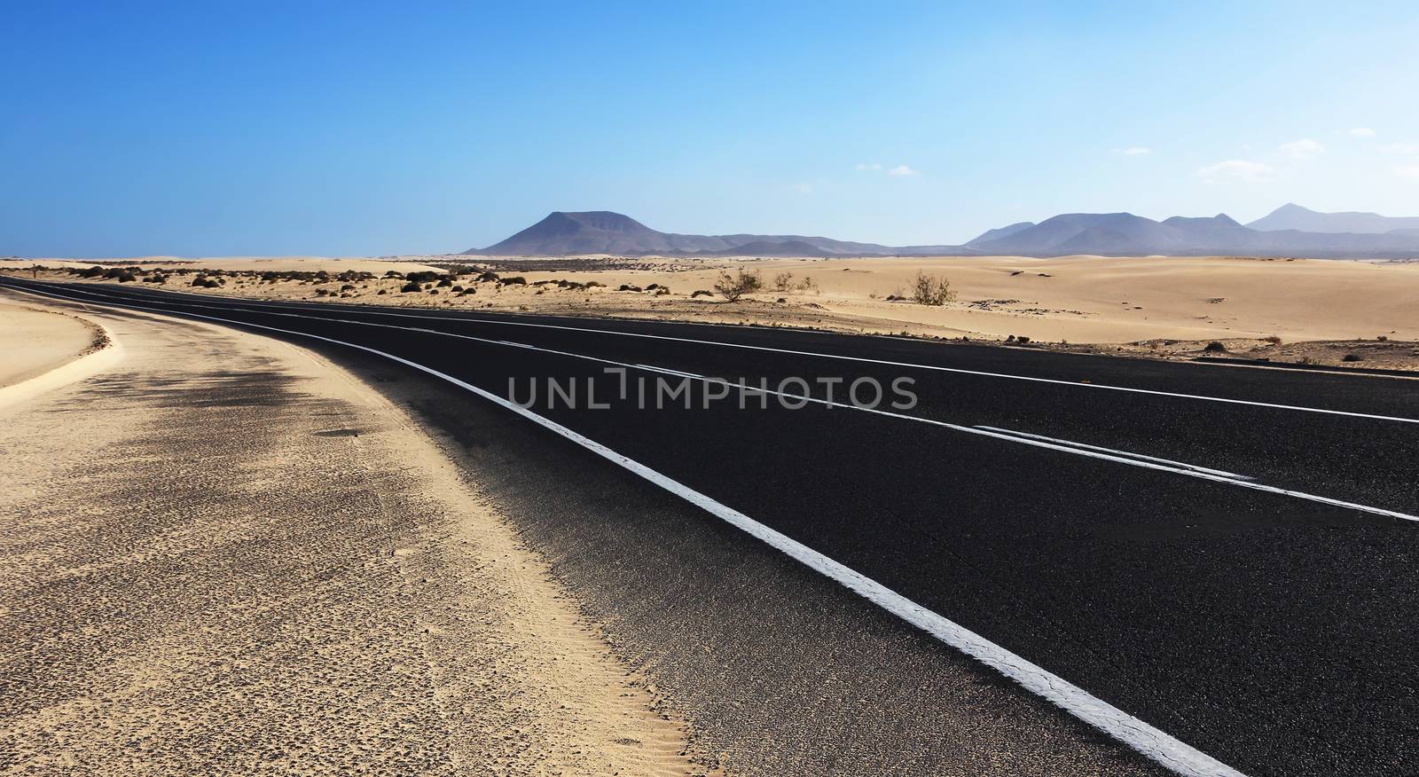Winding road through the dunes of Corralejo desert with volcano in the background, in Fuerteventura, Canary Islands, Spain.