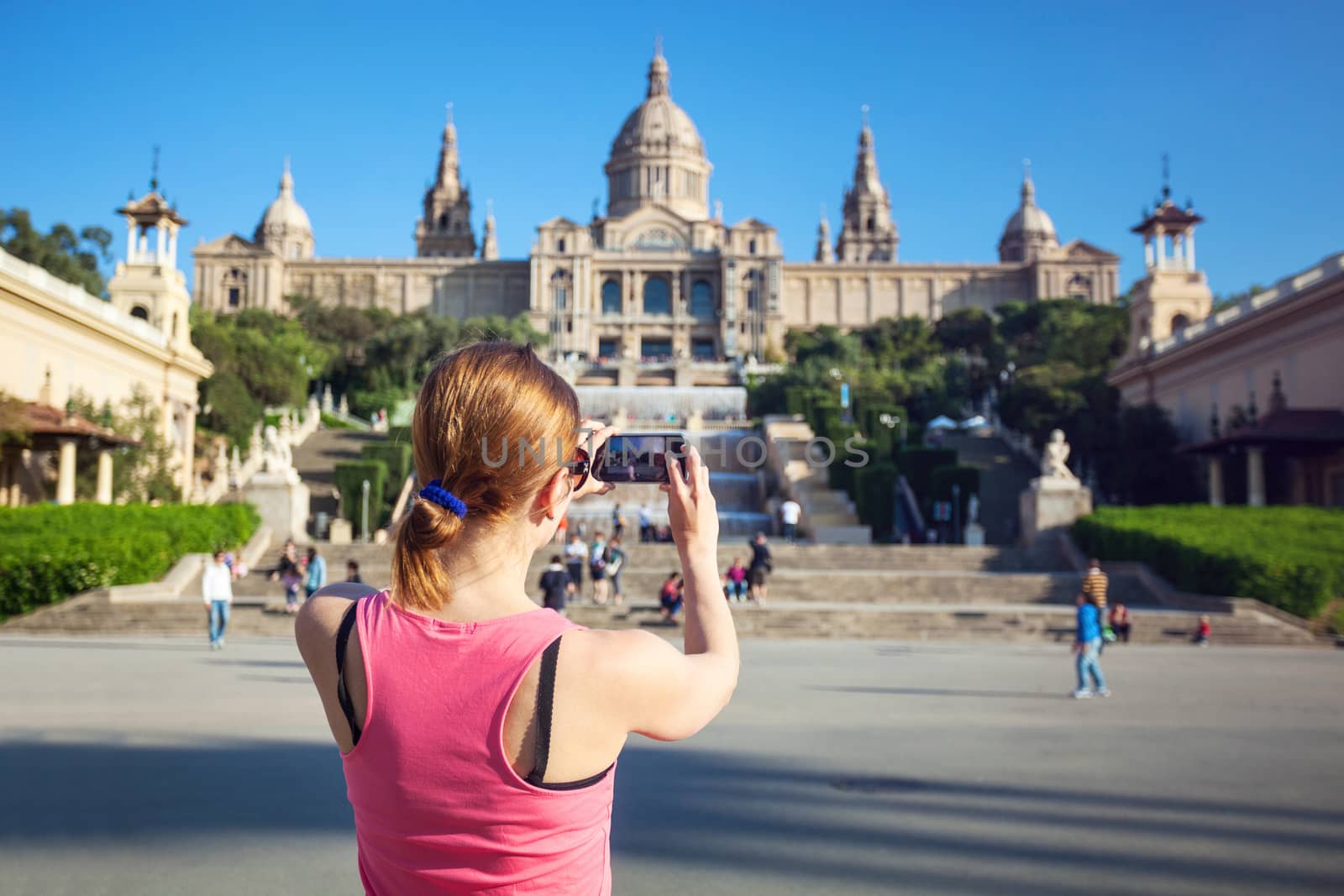 Young woman taking picture of Catalan National Art Museum (MNAC), housed in the Palau Nacional dating to 1929 will mobile phone. Barcelona, Spain.