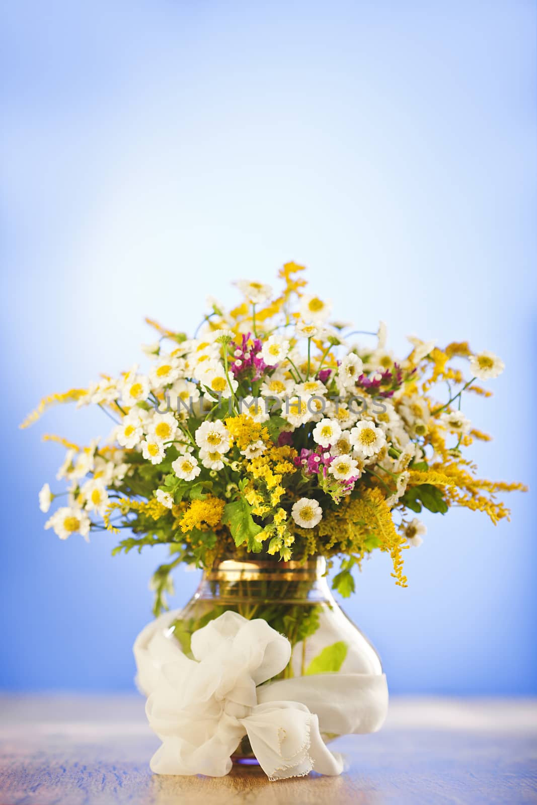 Beautiful bouquet of wildflowers in vase on blue background